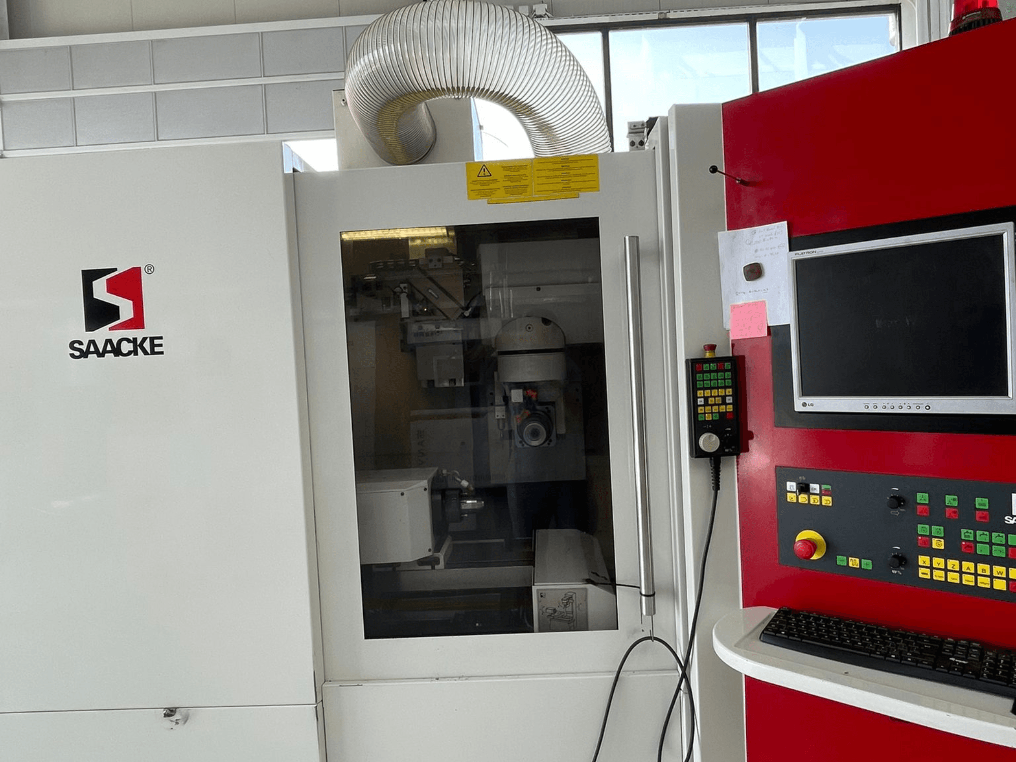 Beyaz ve kırmızı SAACKE makinesi, önden görünüm, kontrol paneli, monitör ve camdan görülebilen iç parçalar.
