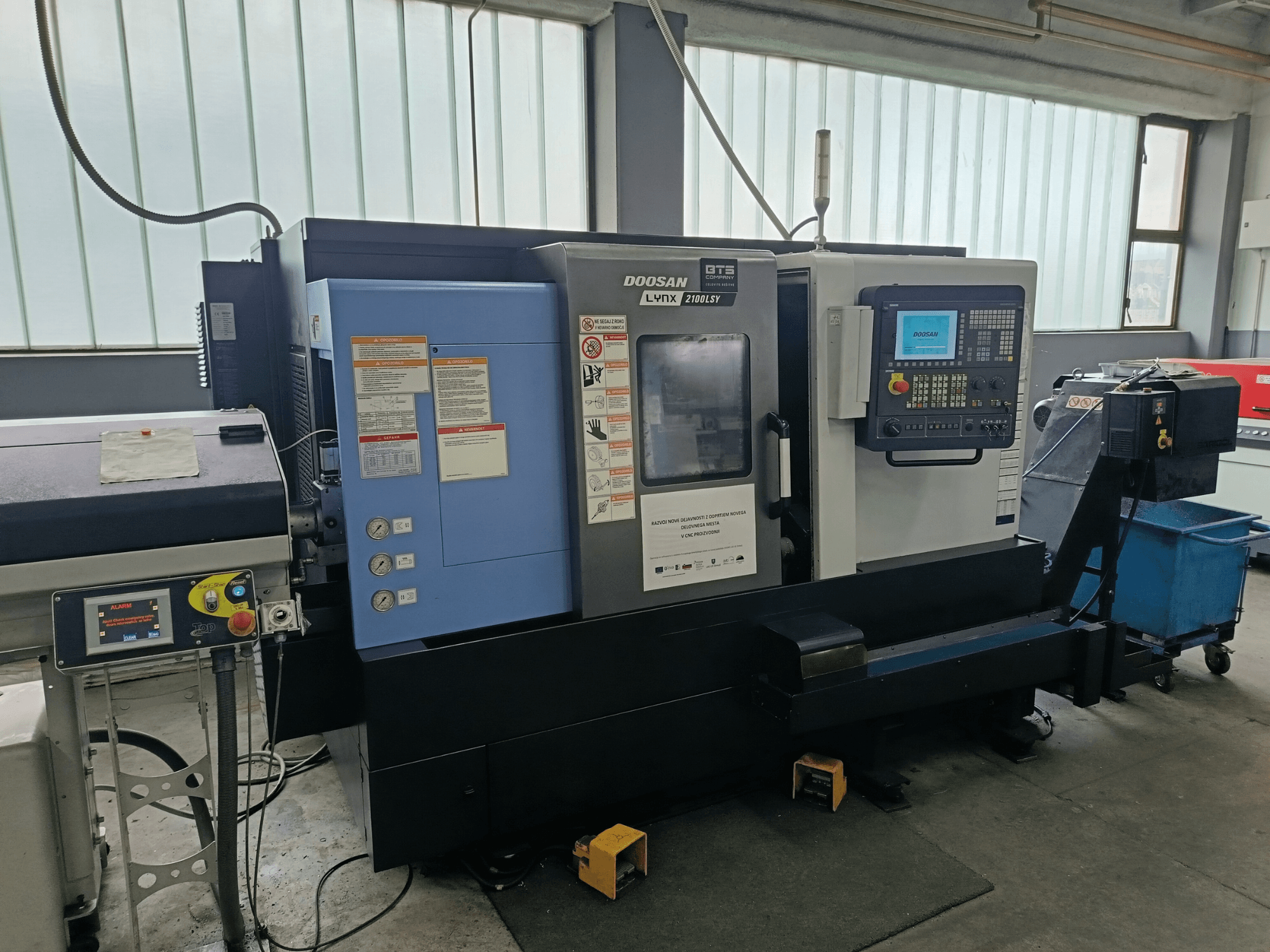 DOOSAN LYNX 2100 LSY Torna Değirmen Merkezi, kontrol panelini ve çalışma düğmelerini gösteren yandan görünüm, bilgi etiketleri görünür.