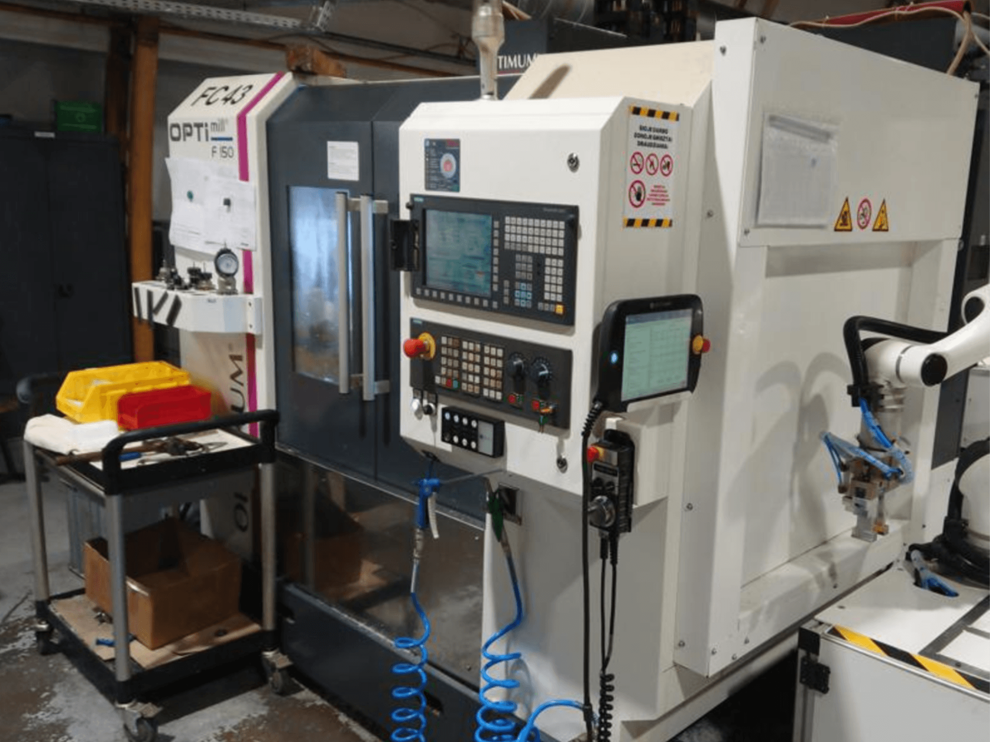 OPTIMUM F50 freze makinesinin kontrol paneli, hortumlar, aletler ve bir atölye ortamında görünen robotik kol.