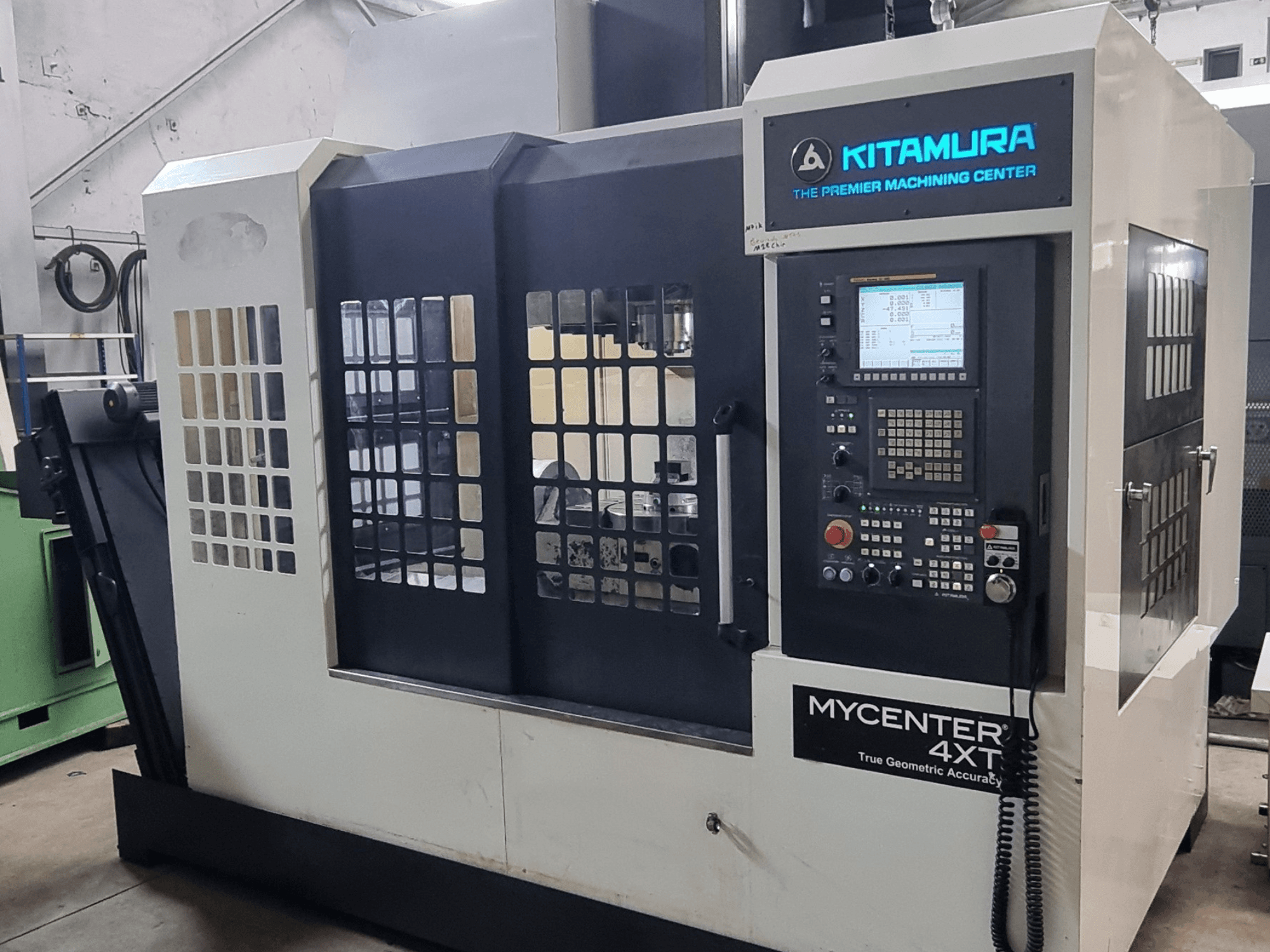 Alternatif metin: Kitamura MYCENTER 4XT dikey işleme merkezi, önden görünüm; bir atölye ortamında kontrol paneli ve makine detayları gösterilmektedir.