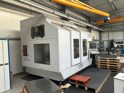 Spinner VC 1650 CNC makinesi, önden görünüm, kontrol paneli, büyük pencereler ve bir atölye ortamında yakınlarda istiflenmiş paletler.