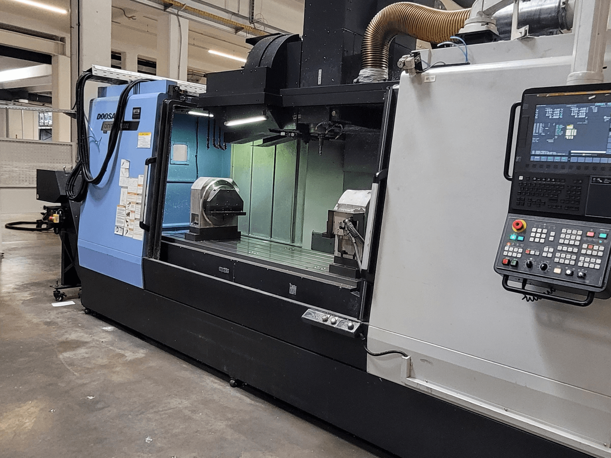 DOOSAN DNM 6700 XL dikey işleme merkezi; kontrol paneli, iş masası ve işleme alanını gösteren önden görünüm.