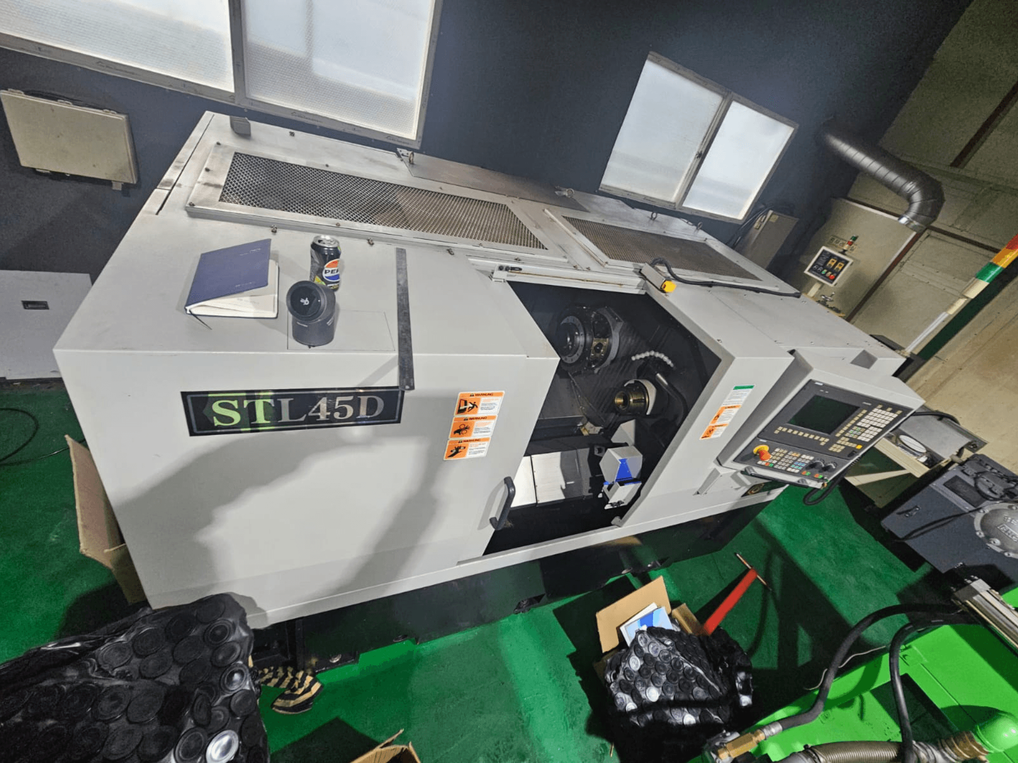 STL45D CNC makinesine yukarıdan bakıldığında kontrol paneli, silindirik parça, dizüstü bilgisayar ve üstte teneke kutu görülmektedir.