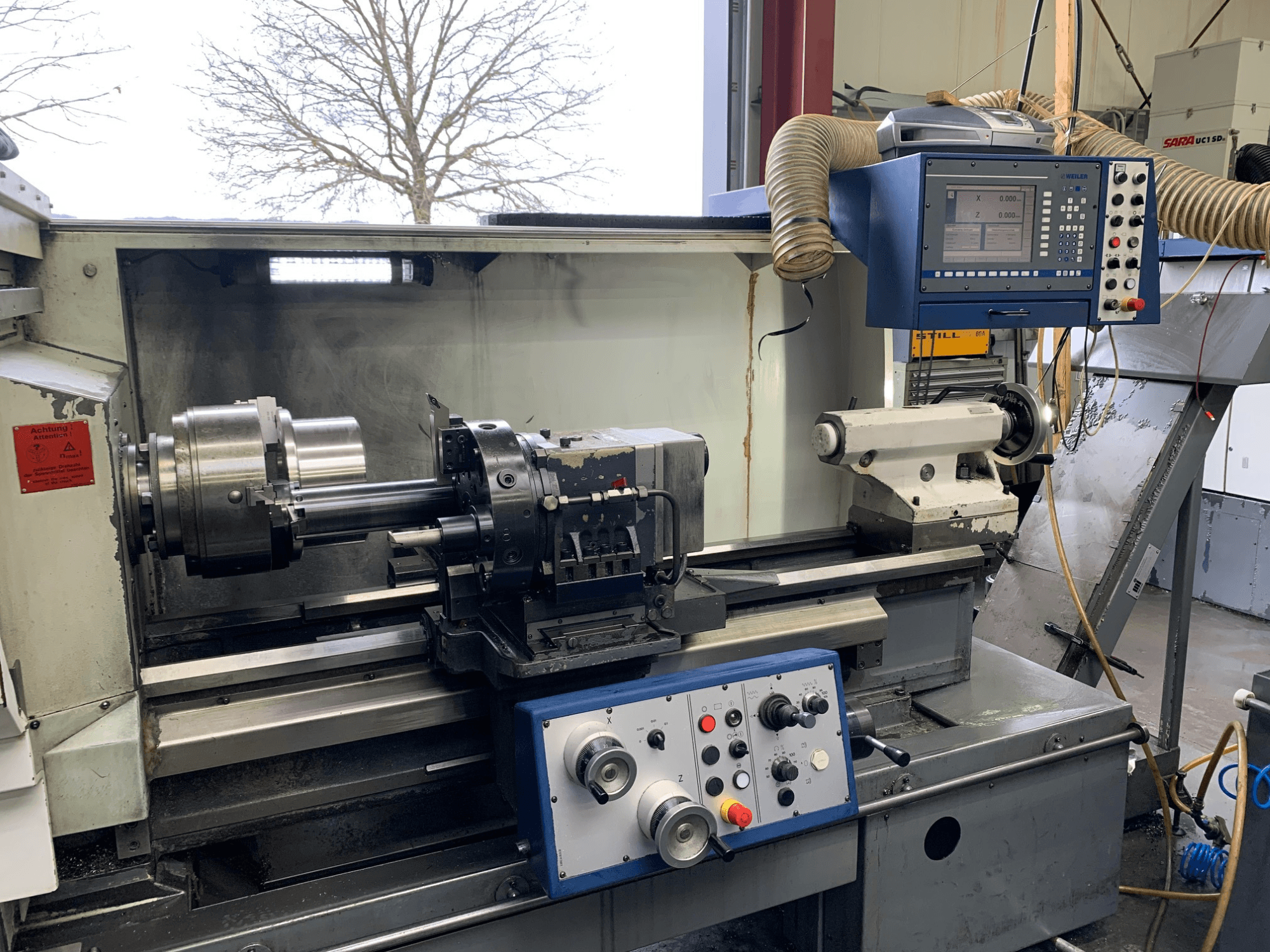 Weiler E55X1000 yatay torna makinesi atölyede, kontrol panelini, torna tezgahını ve takım tutucuyu gösterir. Önden görünüm.