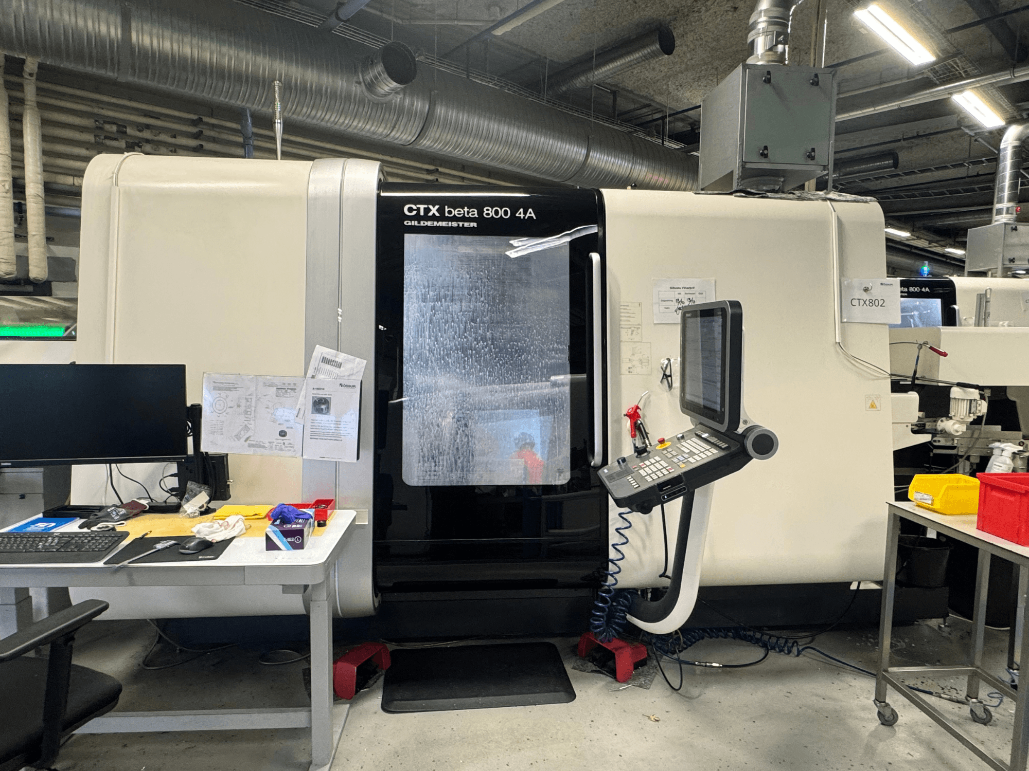 Bir atölyede CTX beta 800 4A CNC makinesi, kontrol panelini ve aletler ve belgelerle dolu çalışma alanını gösteren yandan görünüm.
