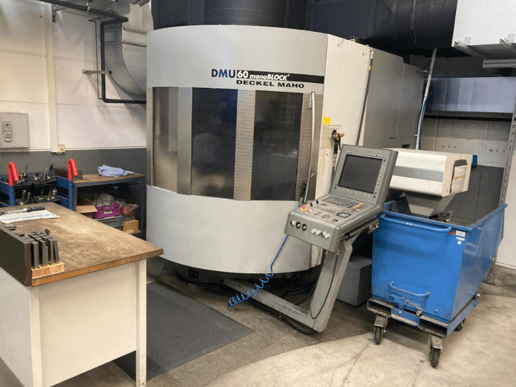 DMG MORI DMU 60 Monoblok dikey işleme merkezi, kontrol paneli, çalışma alanı ve mavi takım arabası görünür şekilde önden görünüm.