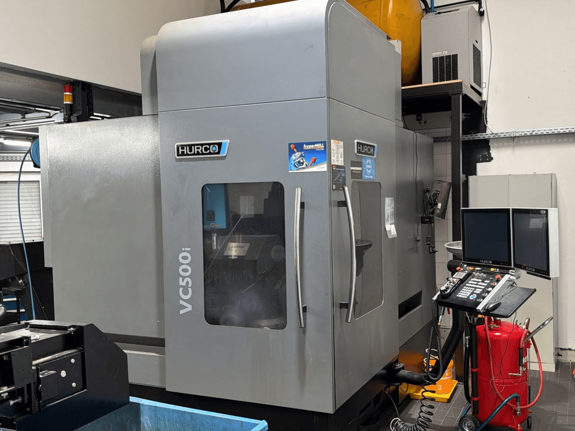 Hurco VC500i dikey işleme merkezi; atölye ortamında, kontrol paneli ve iki monitörün görüldüğü önden görünüm.