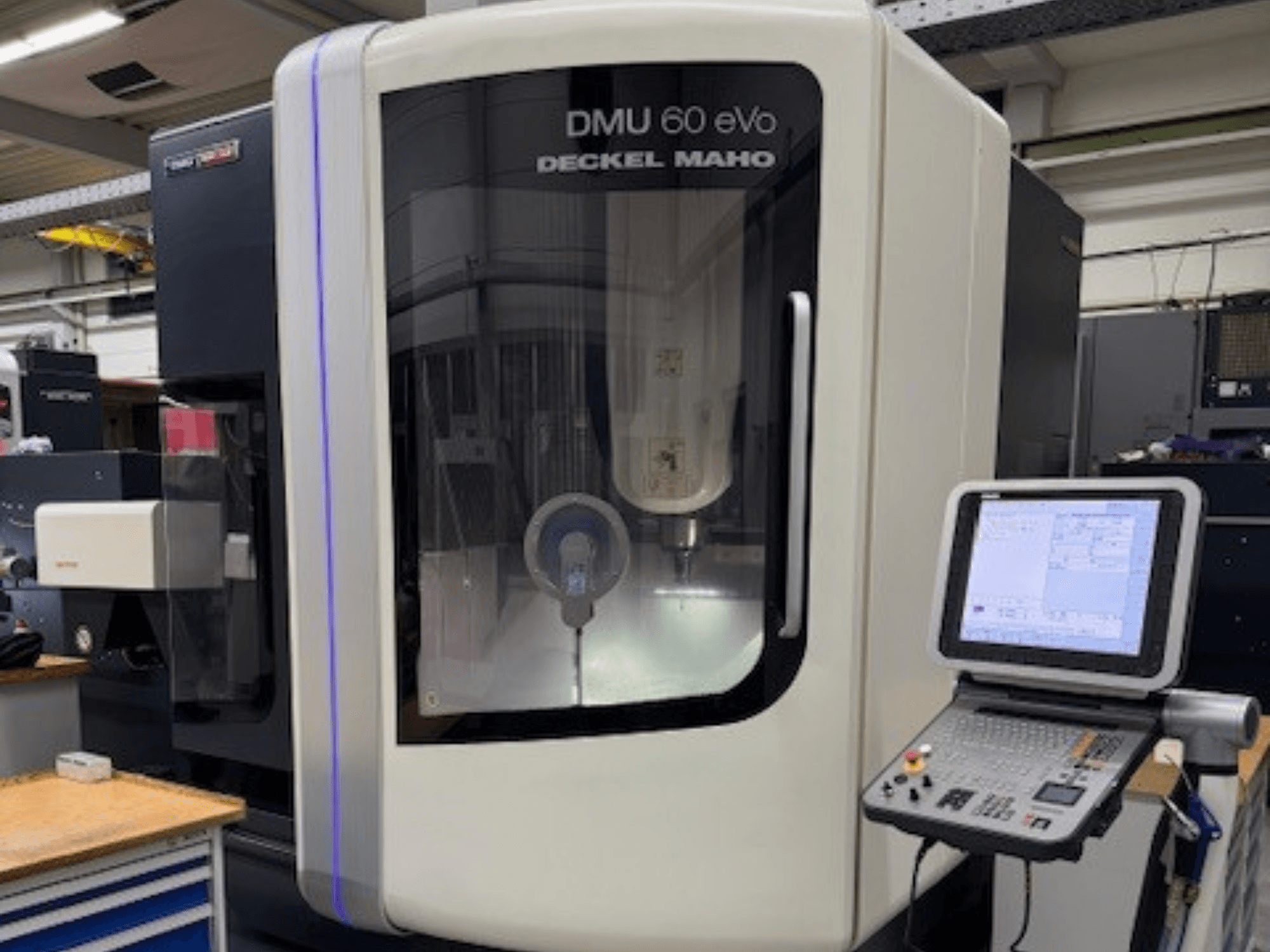 DECKEL MAHO'dan DMU 60 eVo, hassas bileşenleri gösteren kontrol paneli ve ekranlı CNC freze makinesinin önden görünümü.