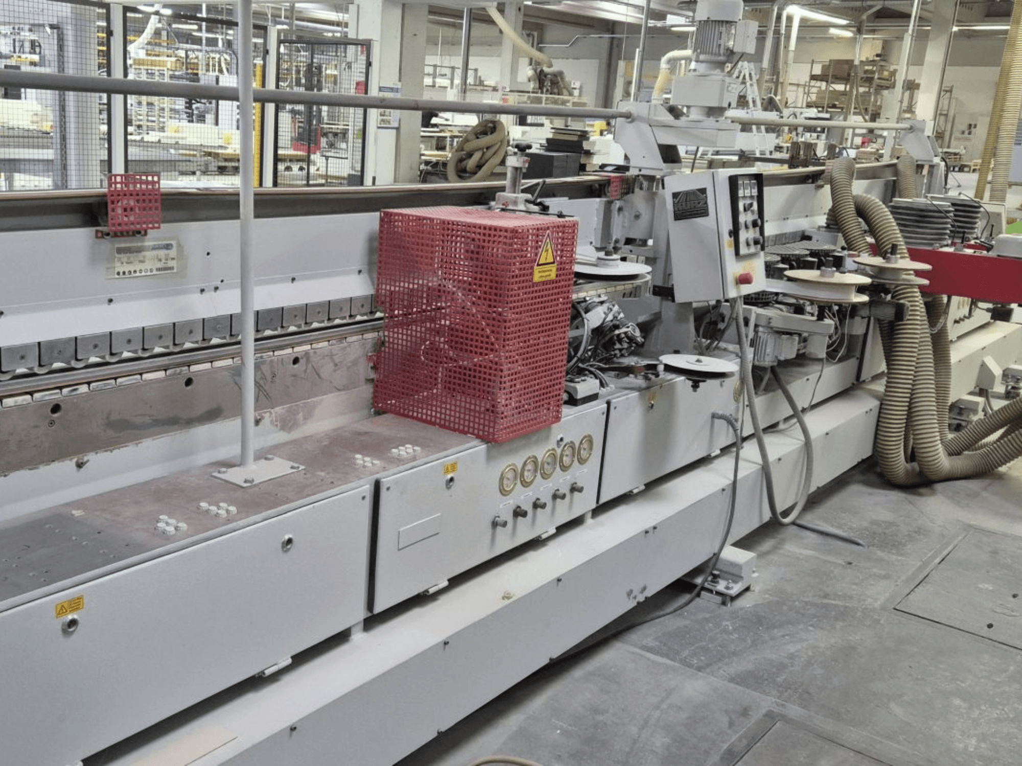 Kontrol paneli, emme hortumları ve kırmızı güvenlik kapağı bulunan kenar bantlama makinesi, yan açıdan görüntülenmiştir.