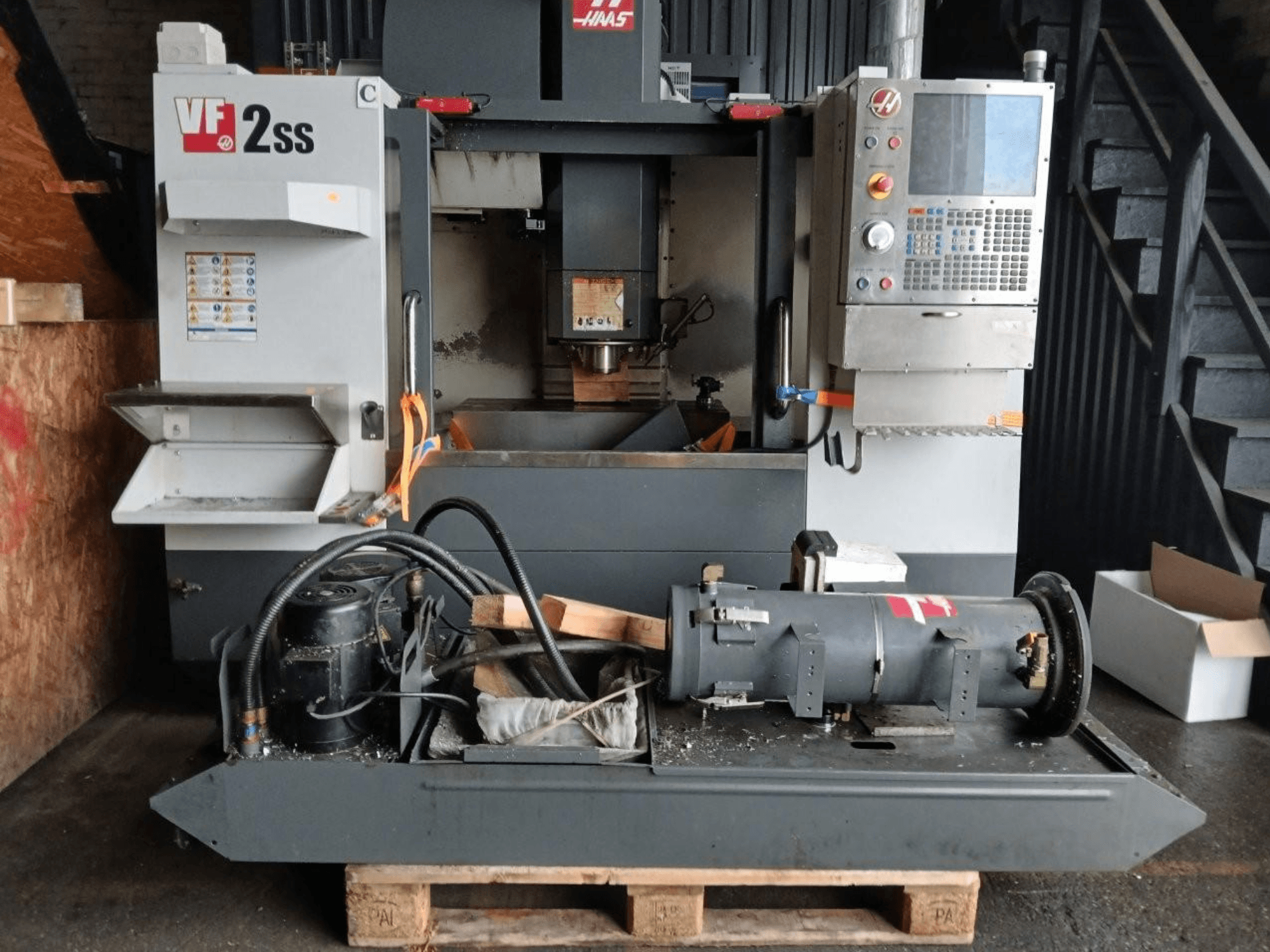 HAAS VF-2SS Dik İşleme Merkezinin önden görünümü, kontrol paneli, iş mili alanı ve bağlı motor bileşenleri.