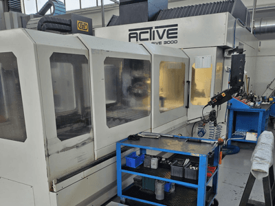 Bir atölyede aktif 3000 CNC makinesi, mavi bir araba üzerindeki aletlerle önden görünüm, görünür kontroller ve içerideki çalışma alanı.