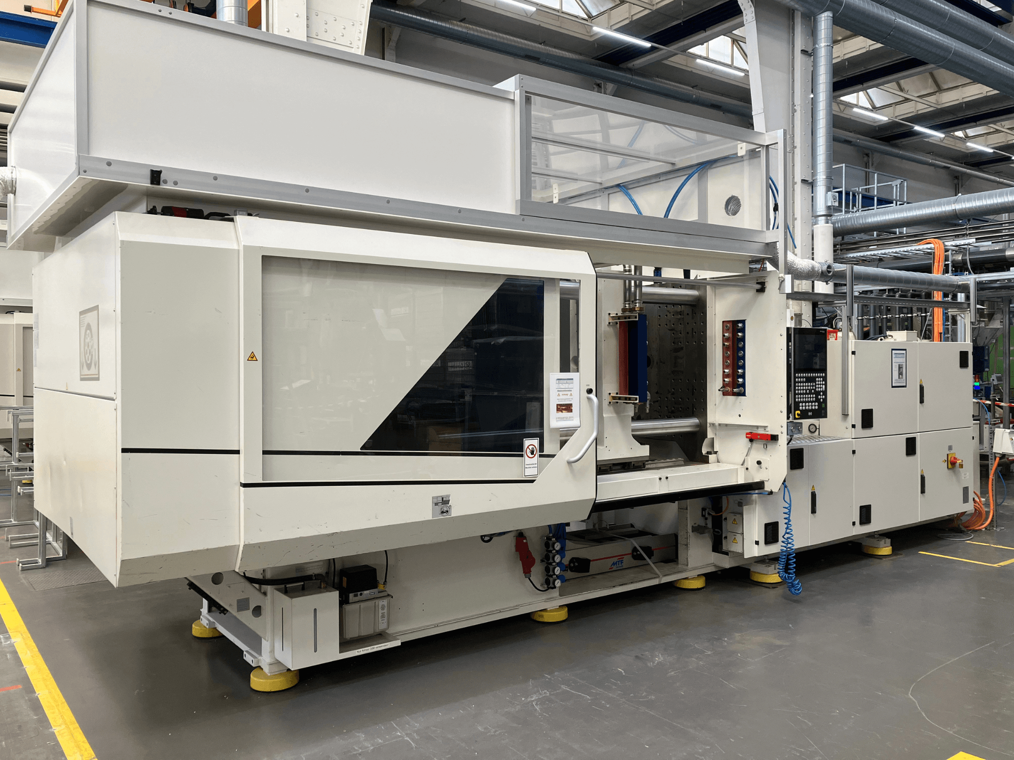 Endüstriyel bir ortamda, kontrol paneli ve şeffaf kapaklara sahip AET model bir enjeksiyon kalıplama makinesinin yandan görünümü.