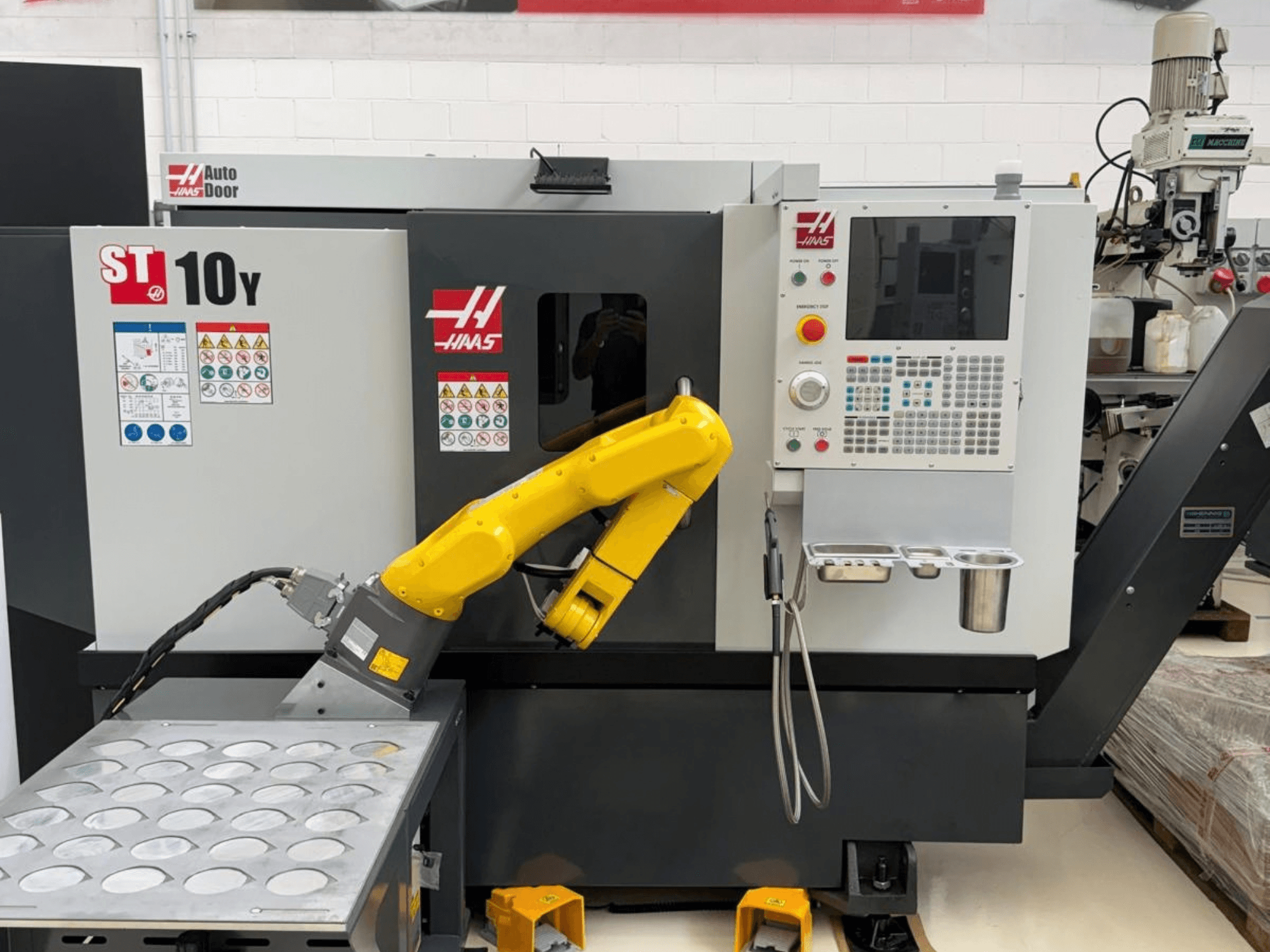 Önden bakıldığında, bir robot kolu ve takım tutucu tepsileri bulunan kontrol paneli ile donatılmış Haas ST-10Y yatay torna tezgahı.
