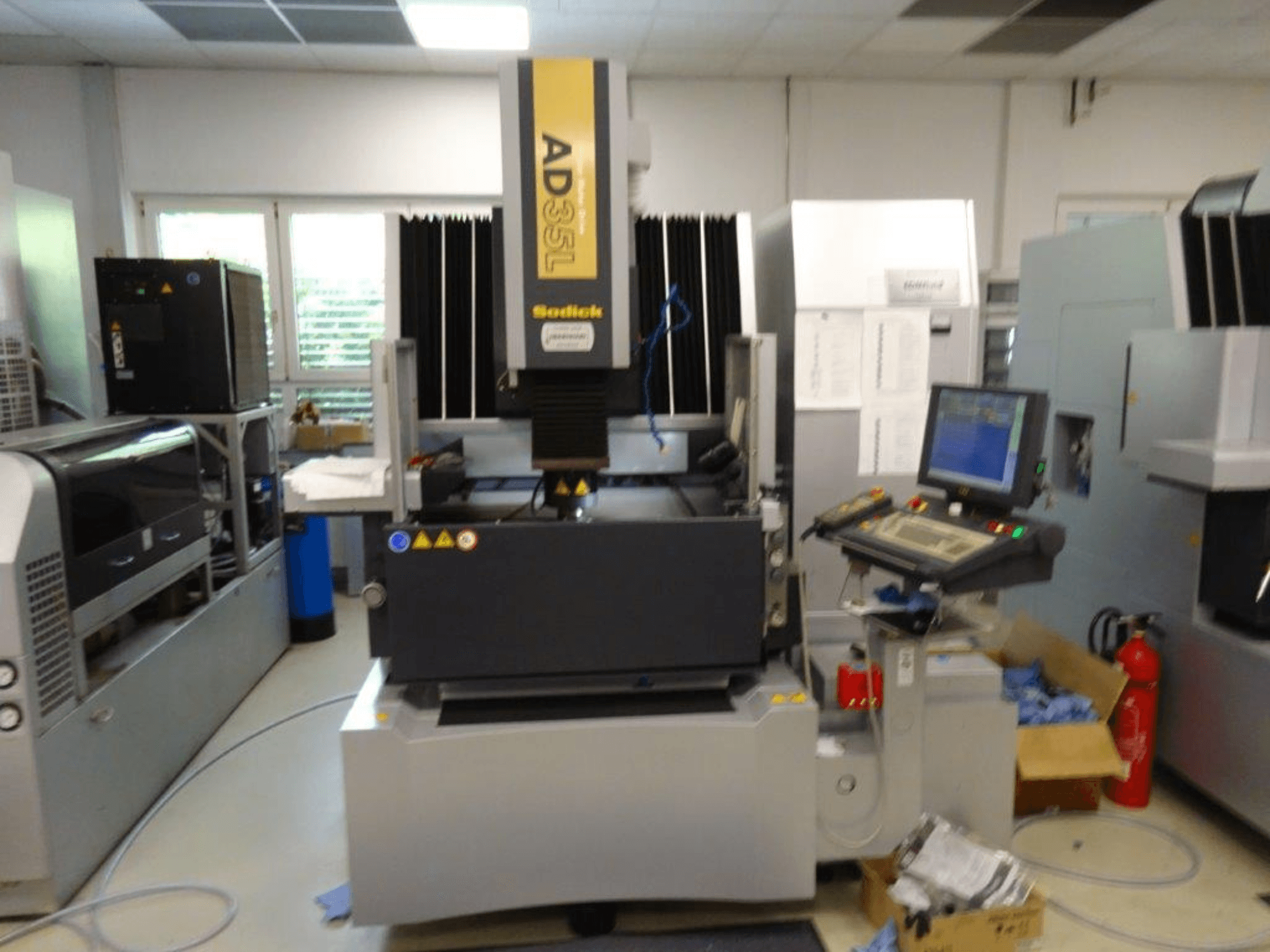 Sodick AD35L CNC makinesinin önden görünümü, kontrol paneli, soğutma ünitesi ve güvenlik göstergeleri.