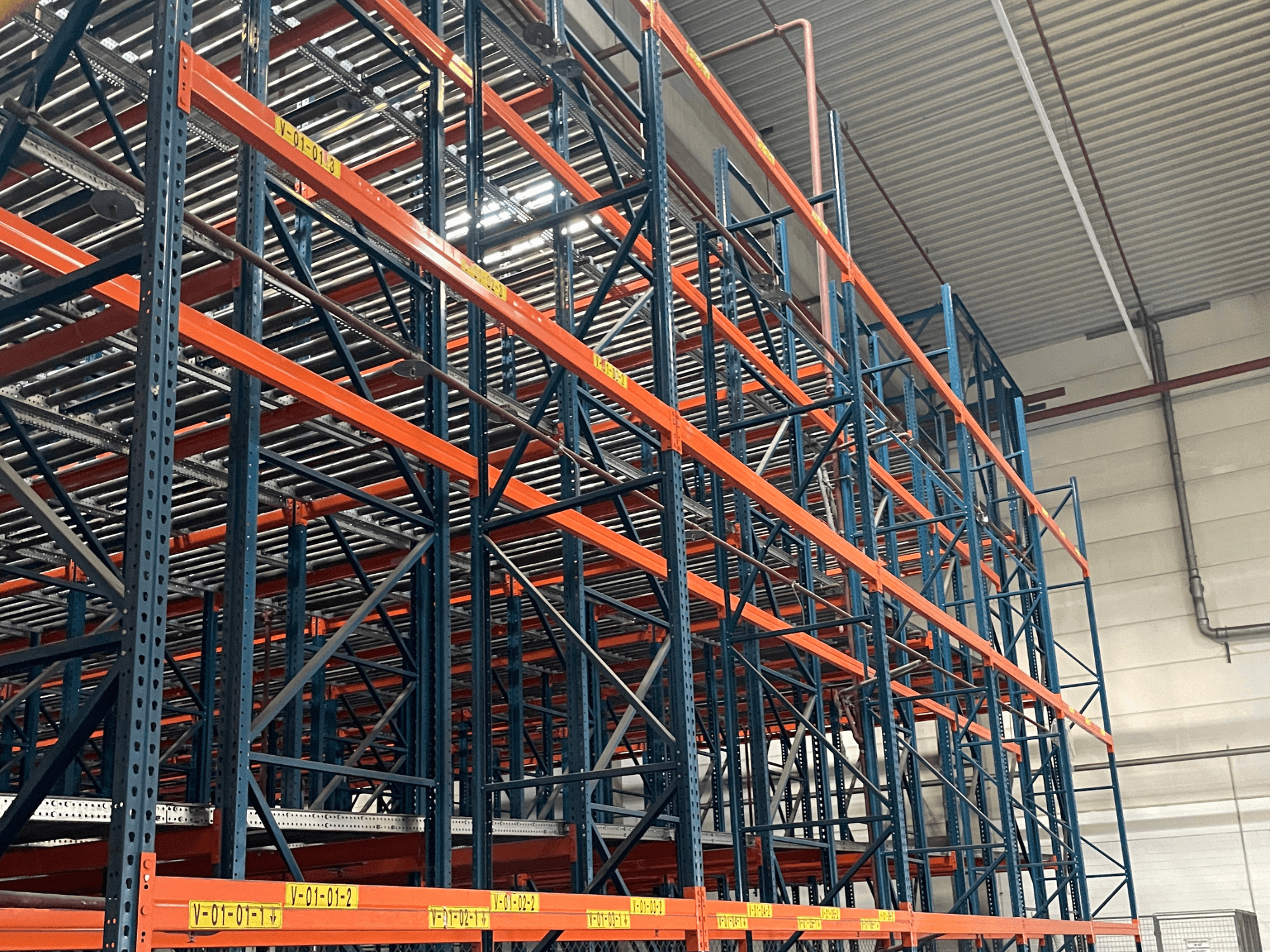 FL SYSTEME F05.10 Bir depodaki FLG palet taşıma sistemi, yandan görünümde, ağır hizmet tipi turuncu ve mavi raflara sahiptir.