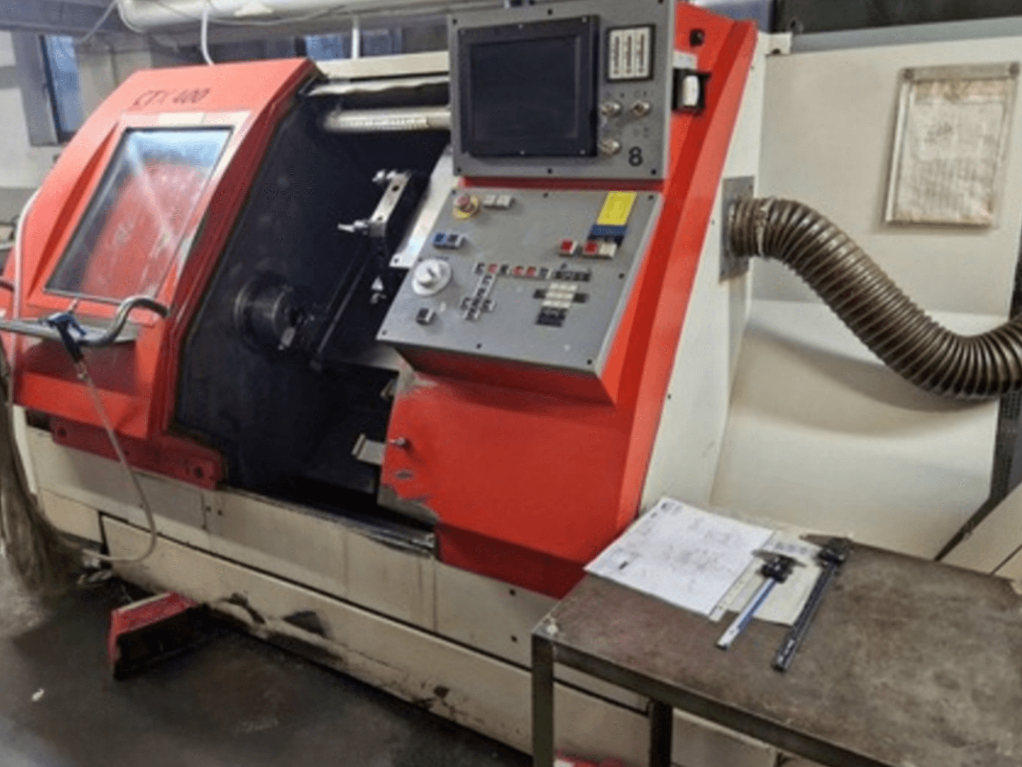 Gildemeister CTX 400 yatay torna makinesi, kontrol paneli ve egzoz hortumu ile önden görünüm. Tabla üzerinde ölçüm aletleri içerir.