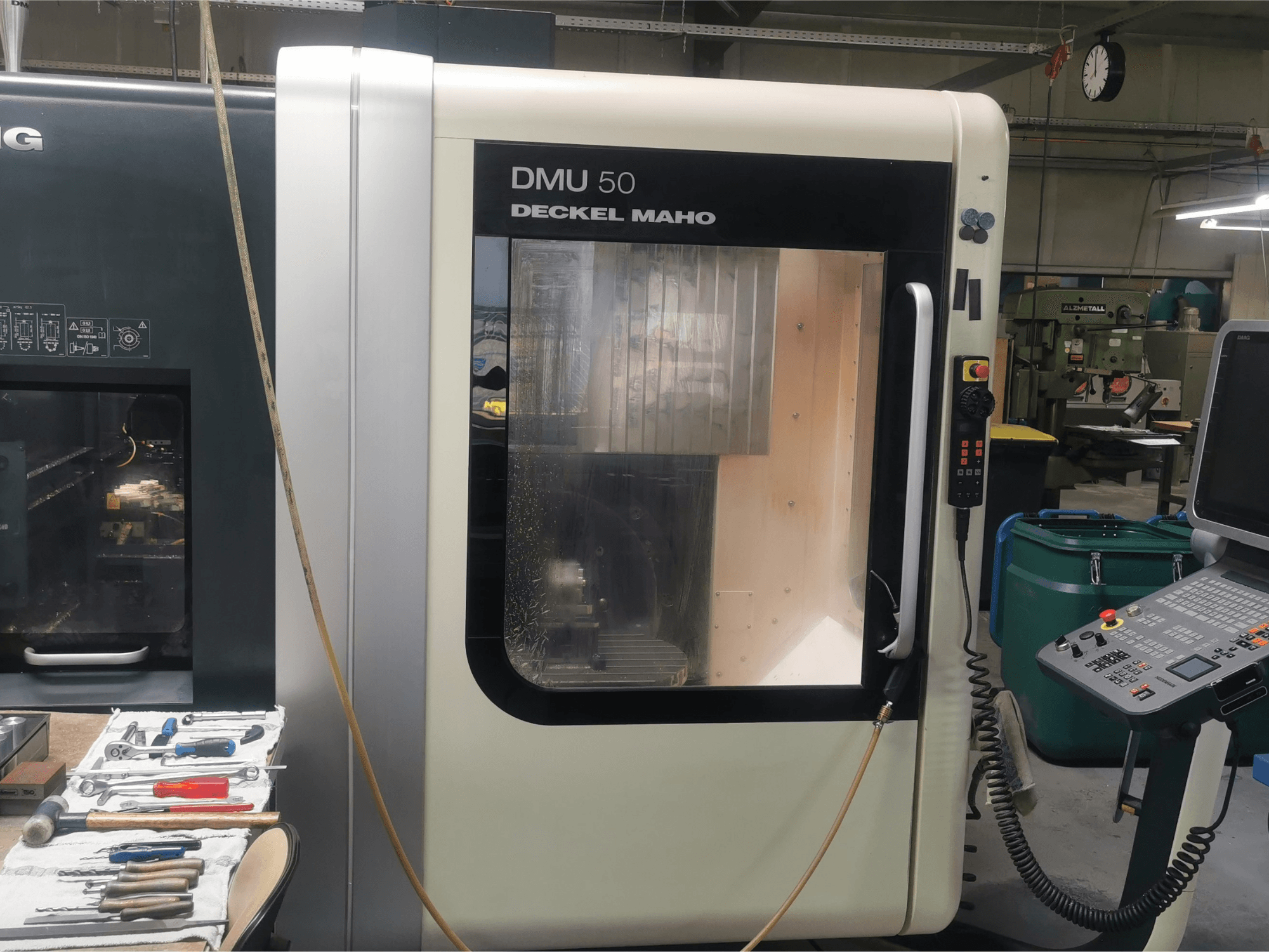 DMU 50 deckel maho CNC makinesi, kontrol panelini ve şeffaf kapısını sergileyerek önden görüntülenmiştir. Aletler yakındadır.