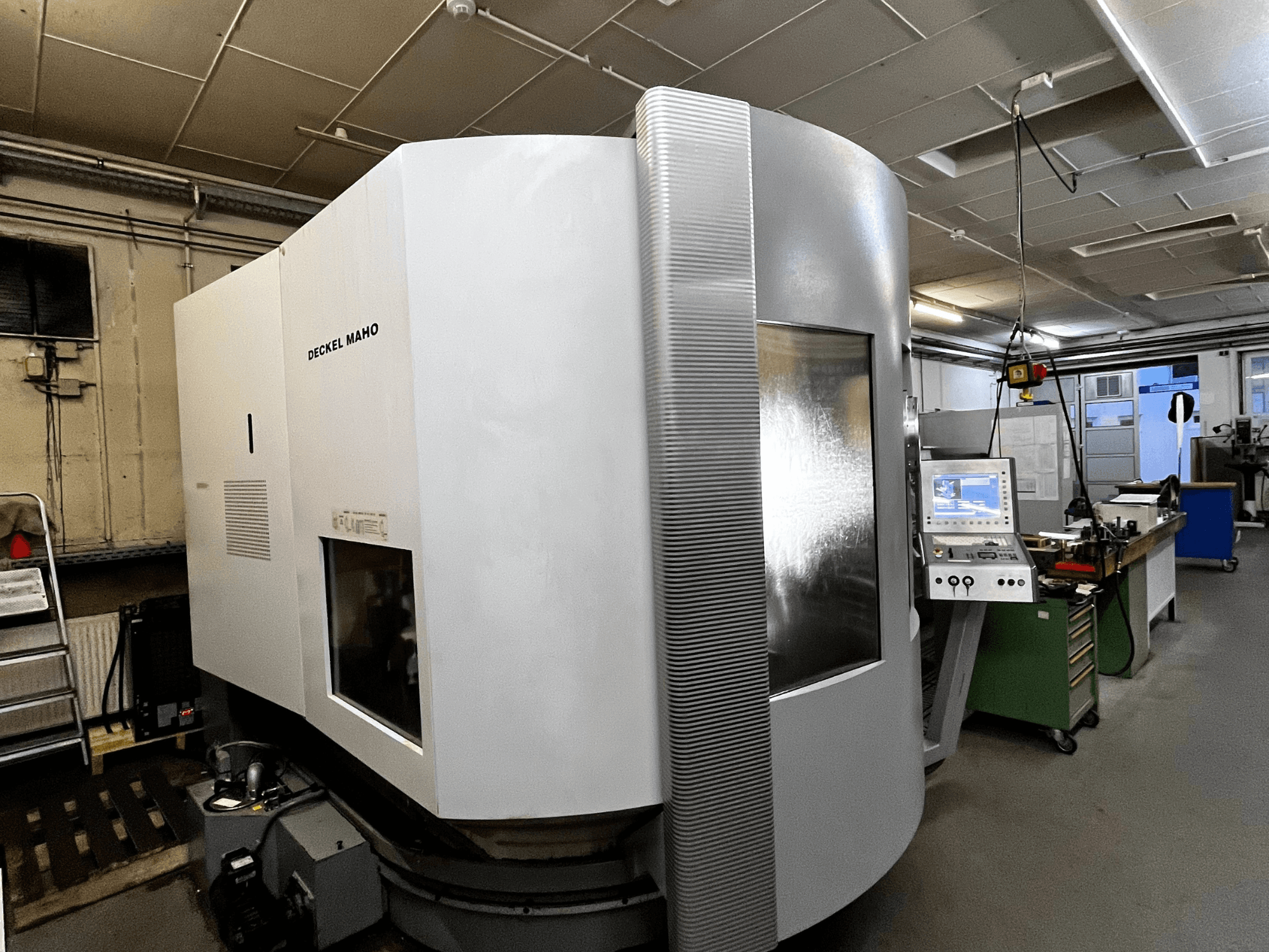 Deckel Maho CNC makinesi, önden görünüm, beyaz dış yüzey, kontrol paneli görünür, atölye ortamı.