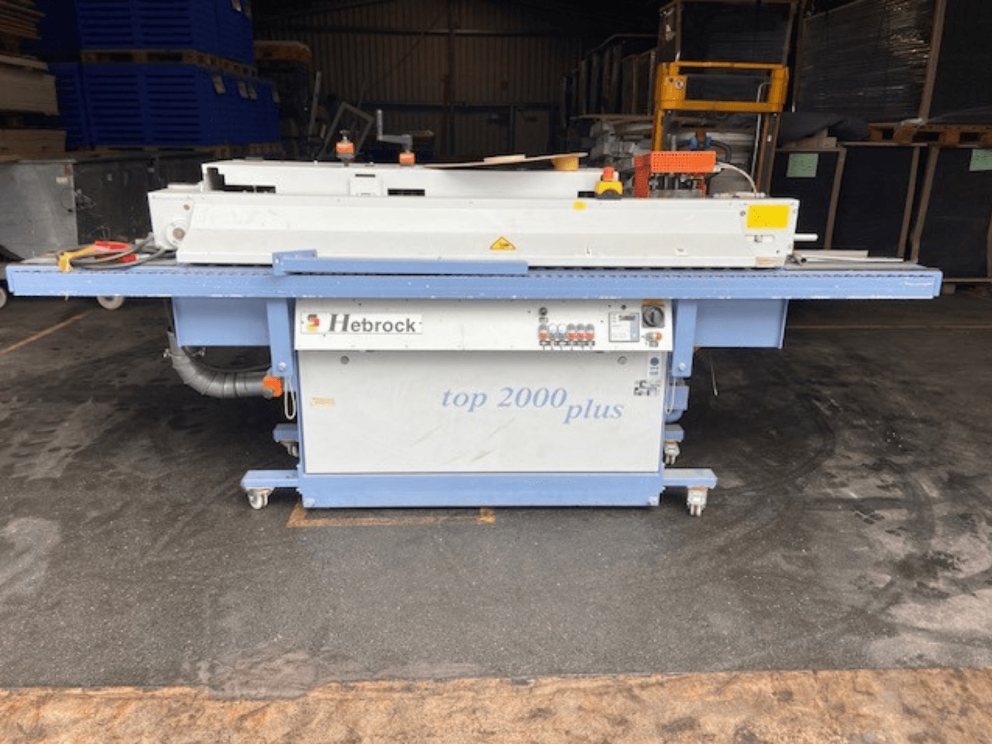 Hebrock Top 2000 Plus, önden görünüm; kontrol paneli, hareket için tekerlekleri ve güvenlik etiketleri görünen endüstriyel elektrikli makine.