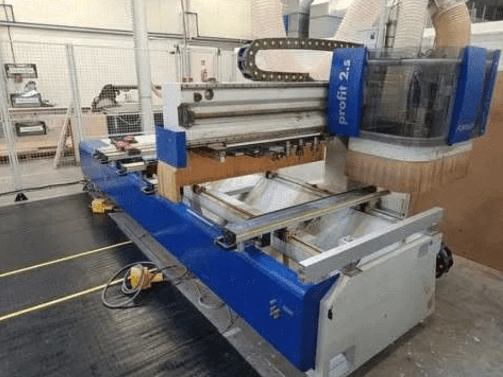 CNC makinesi, Profitec 2.5 marka, önden görünüm mavi gövdeyi, çalışma alanını ve ahşap işleme için toz emme nozülünü göstermektedir.