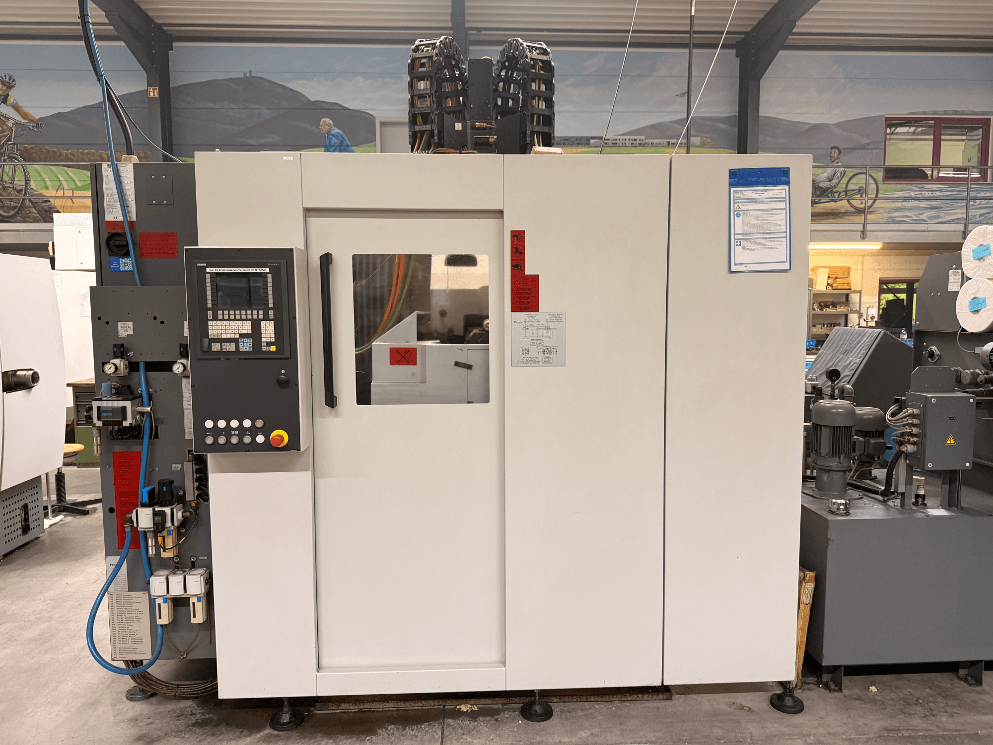 Kontrol panelli beyaz CNC işleme merkezi, önden görünüm, düğmeler ve dijital ekran, bir atölye ortamında.
