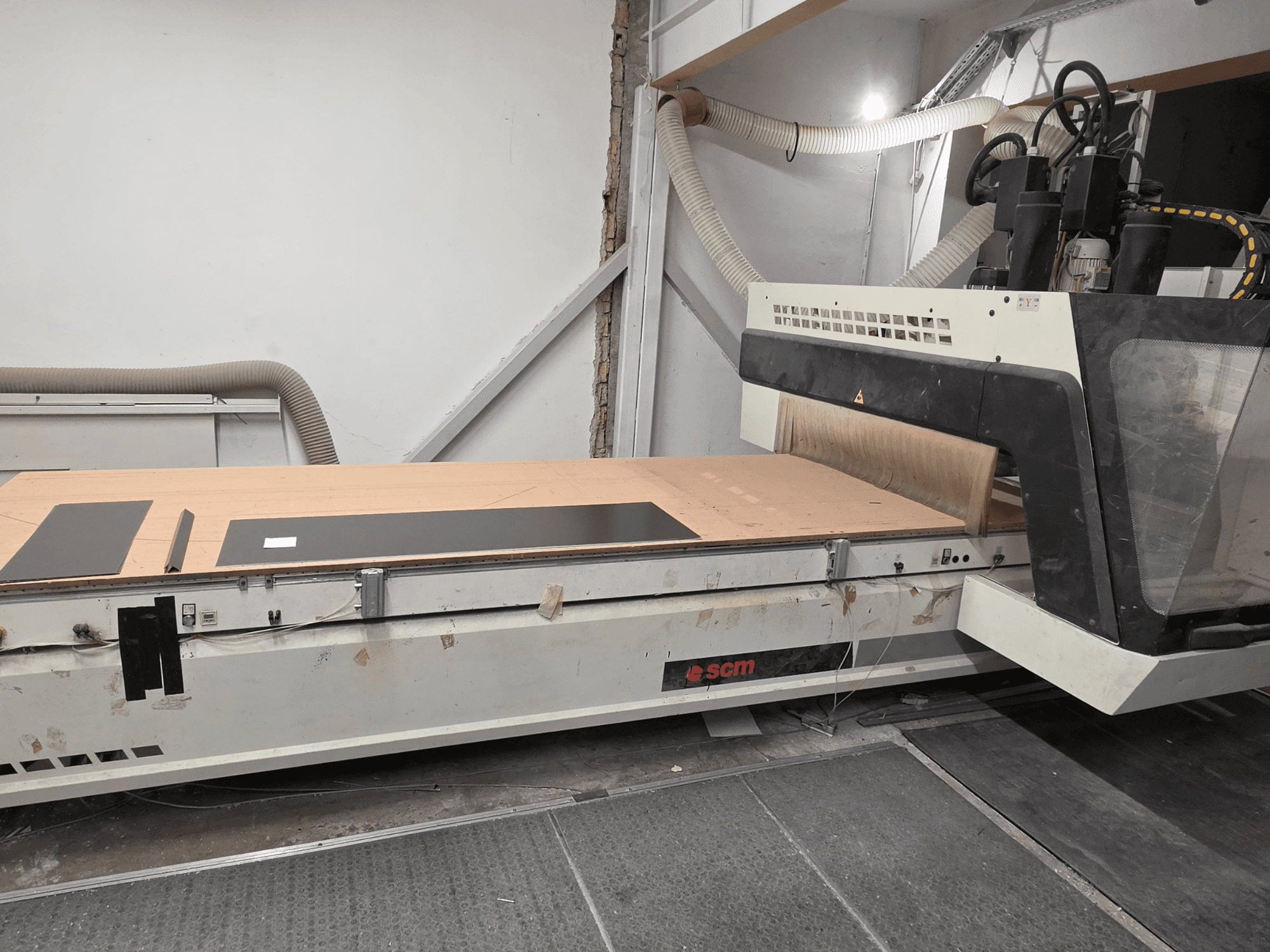 SCM RECORD 132 CNC ahşap işleme merkezinin yandan görünümü; düz bir çalışma masası, siyah iş parçaları ve toz toplama sistemi ile donatılmıştır.