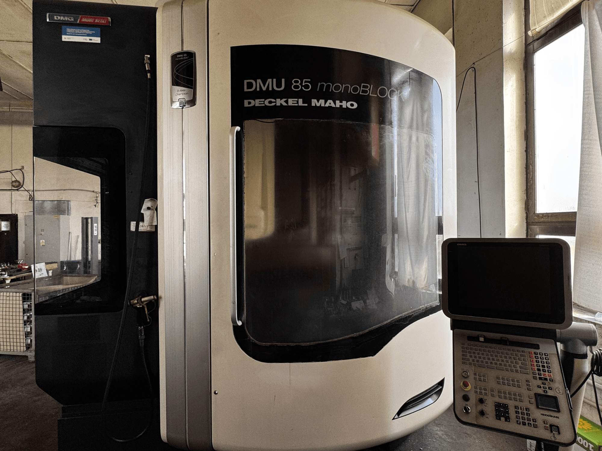DMG MORI DMU 85 monoBLOCK dik işleme merkezi, kontrol paneli ve geniş izleme penceresi ile önden görünüm.
