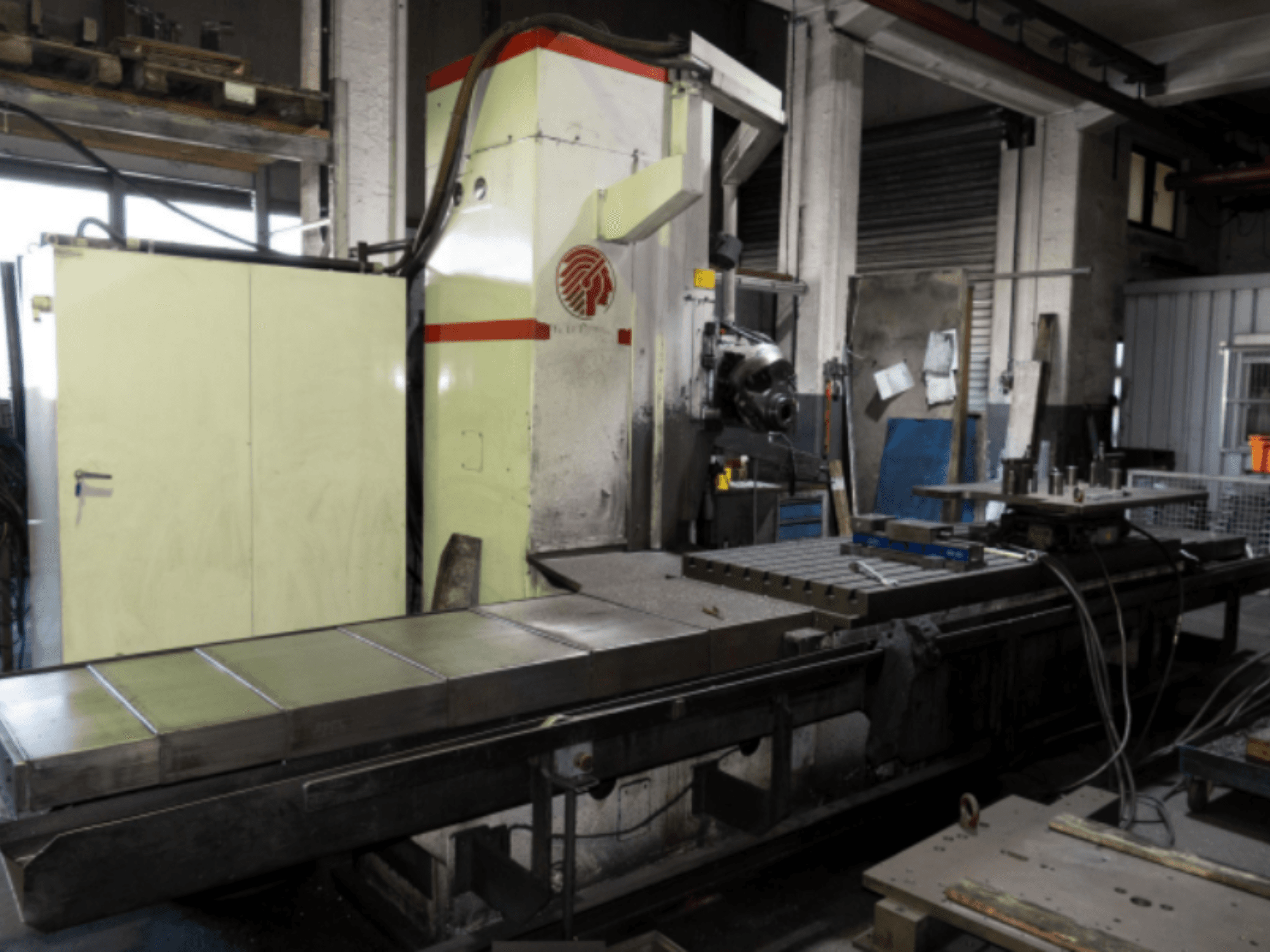 Büyük tablalı endüstriyel freze makinesi, yandan görünüm, atölye ortamında kontroller ve ataşmanlar sergileniyor.