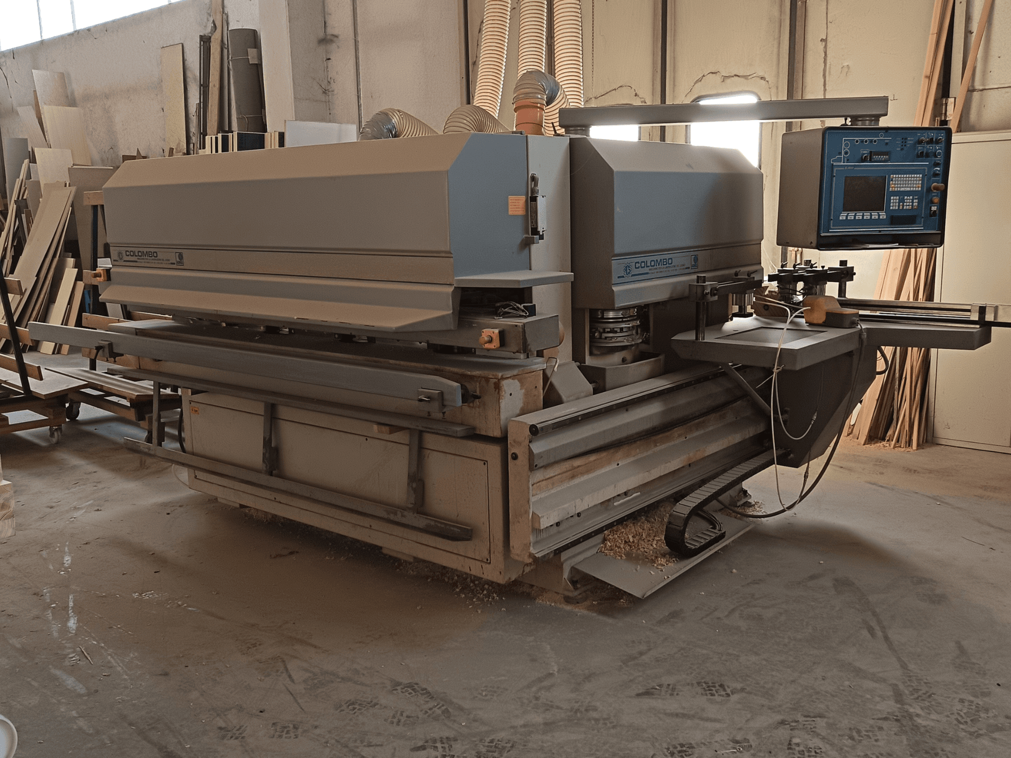 Colombo ahşap işleme makinesi, yandan görünüm, kontrol paneli, kesme bıçakları ve atölyede testere tozu birikimi.