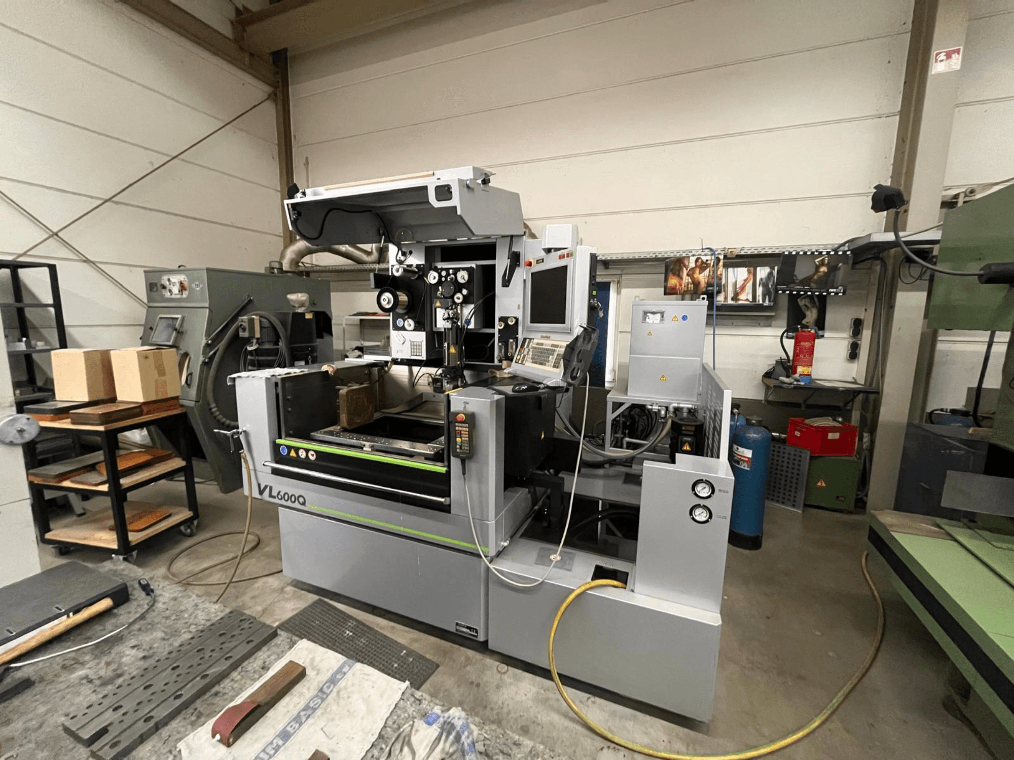 Atölyede VL600Q CNC makinesi, önden görünüm, kontrol paneli, yerinde malzeme ve yanında çeşitli aletler.