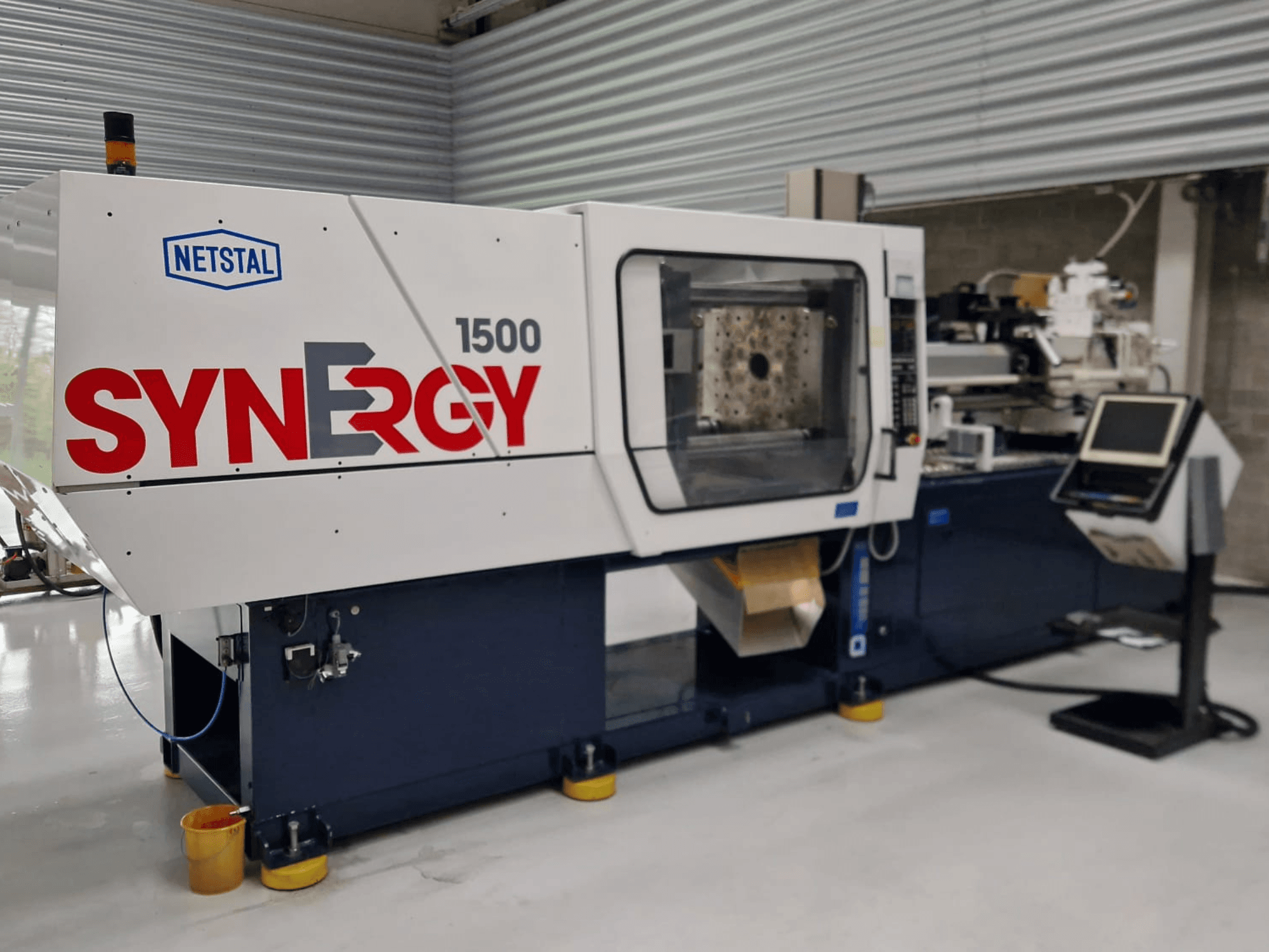 Netstal Synergy 1500-460 hidrolik enjeksiyon kalıplama makinesi, önden görünüm, kontrol paneli ve açık enjeksiyon alanı.