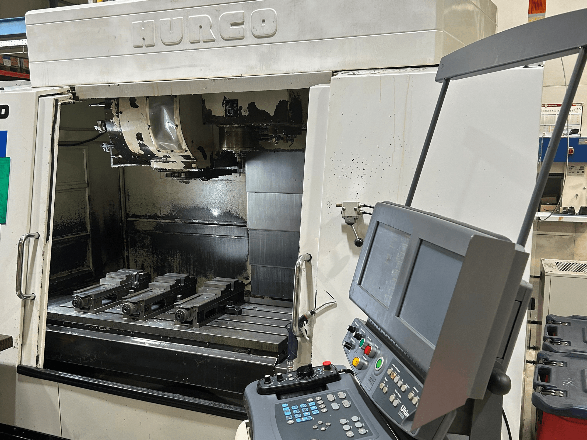 Hurco CNC freze makinesi, önden görünüm, tabla üzerinde dört takım tutucu ve çift ekran ve düğmeler içeren bir kontrol paneli.