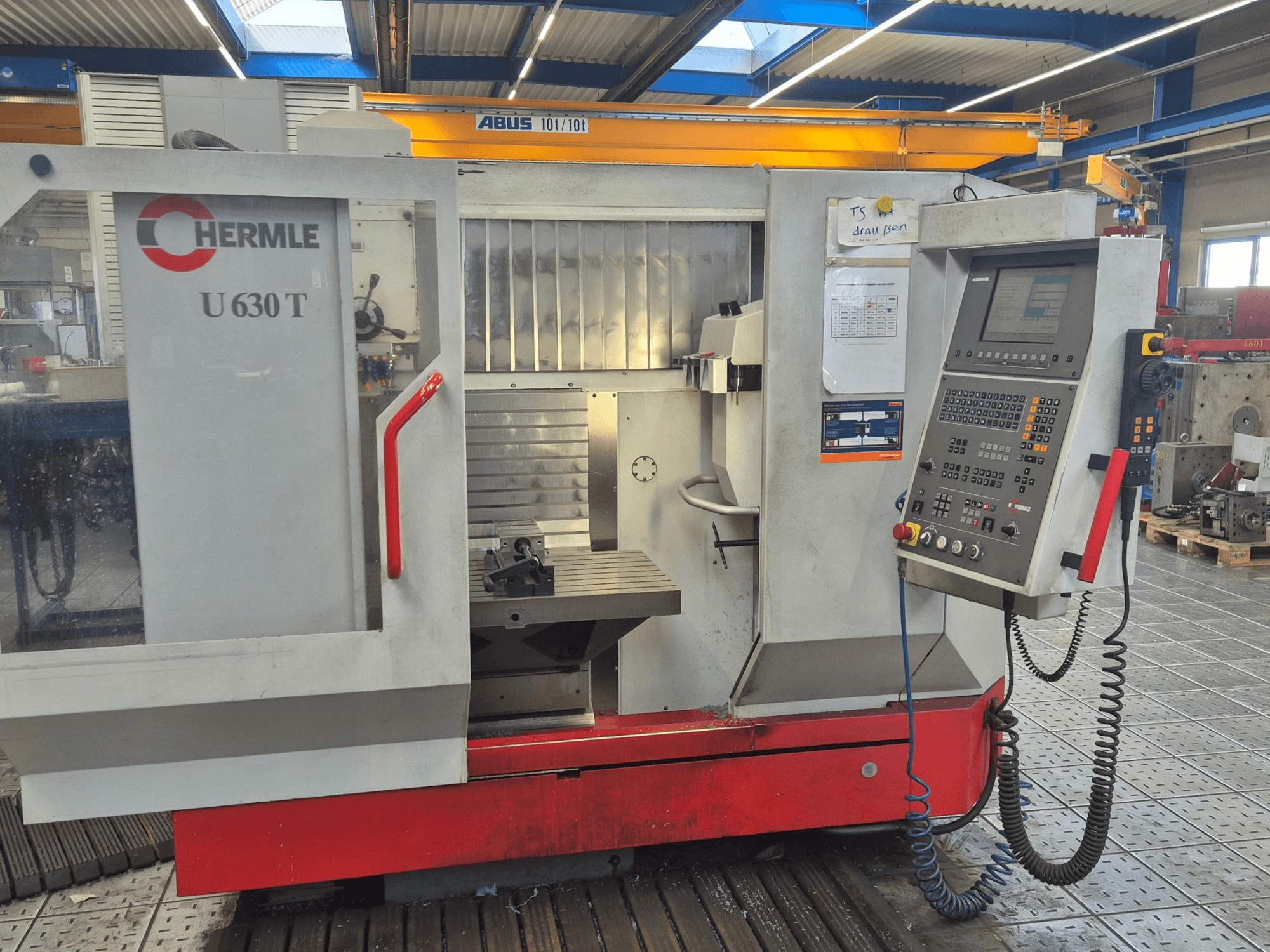 HERMLE U 630 T dikey işleme merkezinin önden görünümü, kontrol paneli, çalışma tezgahı ve güvenlik muhafazası.
