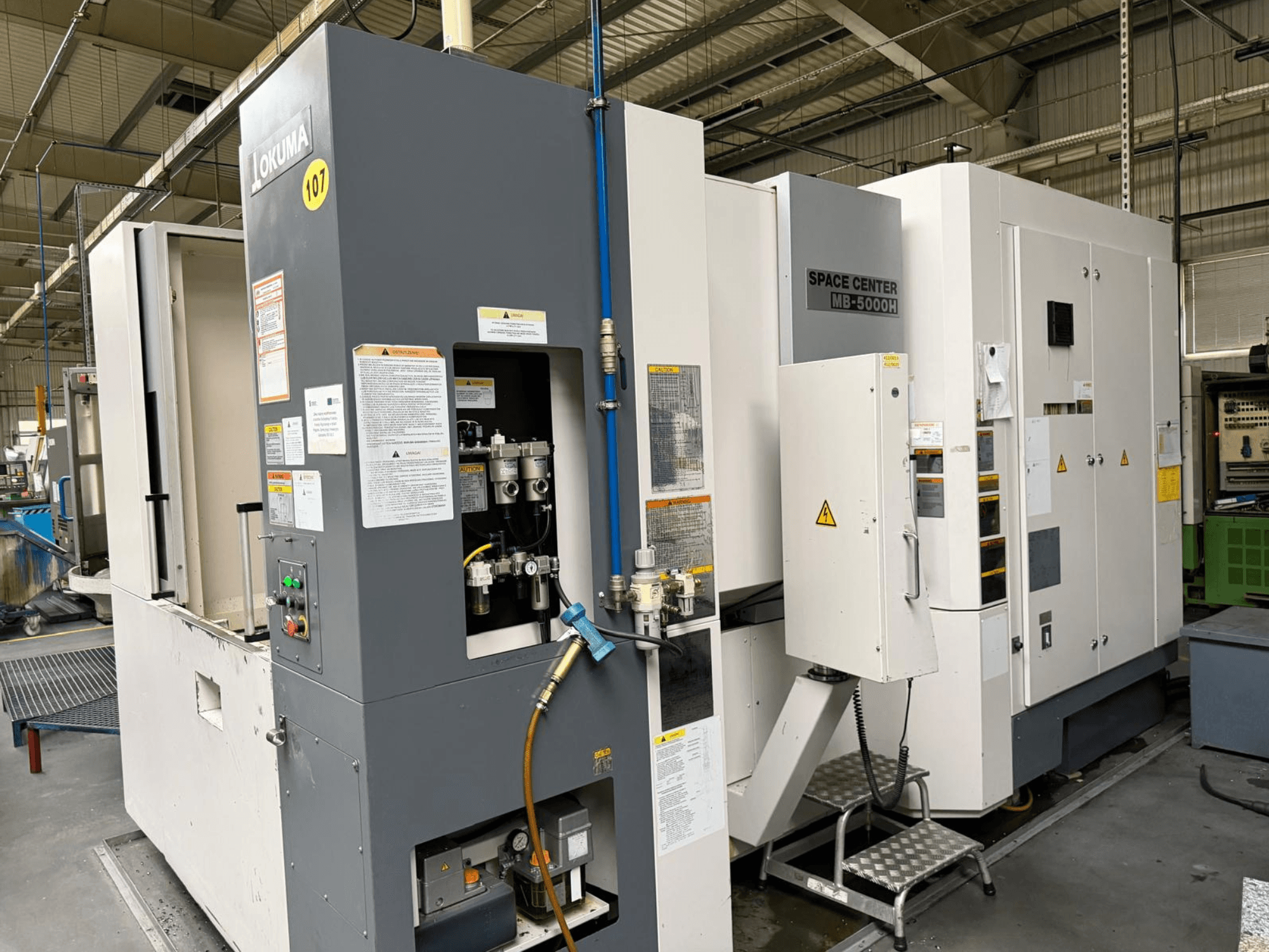 Okuma MB 5000H yatay işleme merkezi, fabrika ortamında kontrol paneli ve makine bileşenlerini gösteren yandan görünüm.