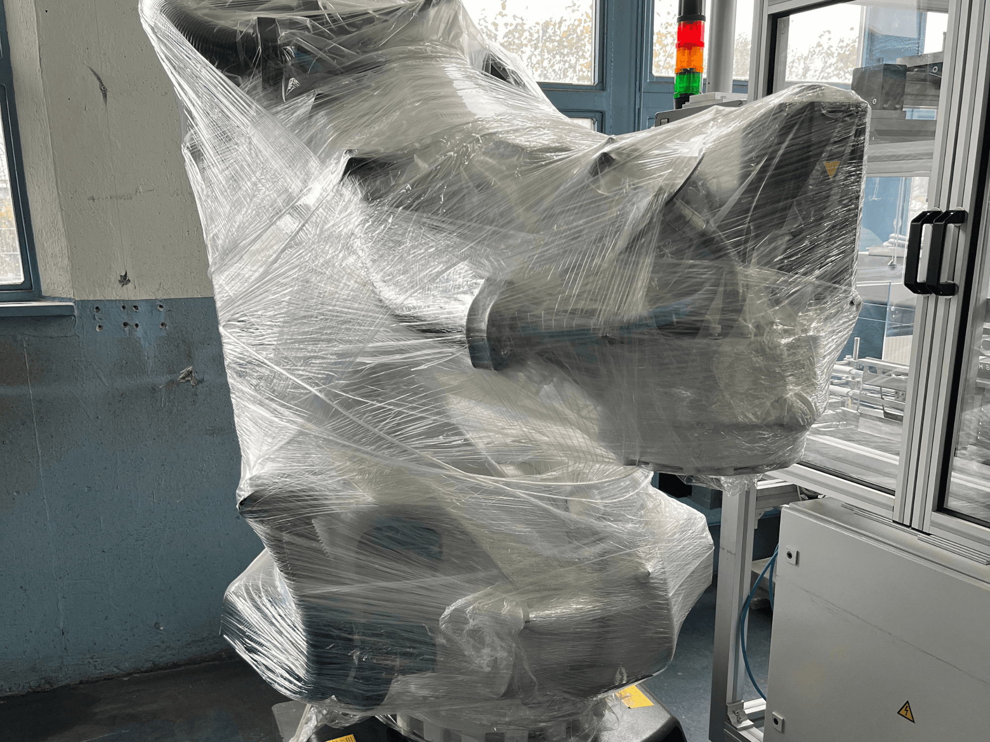 Plastikle sarılmış endüstriyel robotik kol, önden görünüm. Kontrol ünitesi ve gösterge ışığı içerir. Marka görünmüyor.