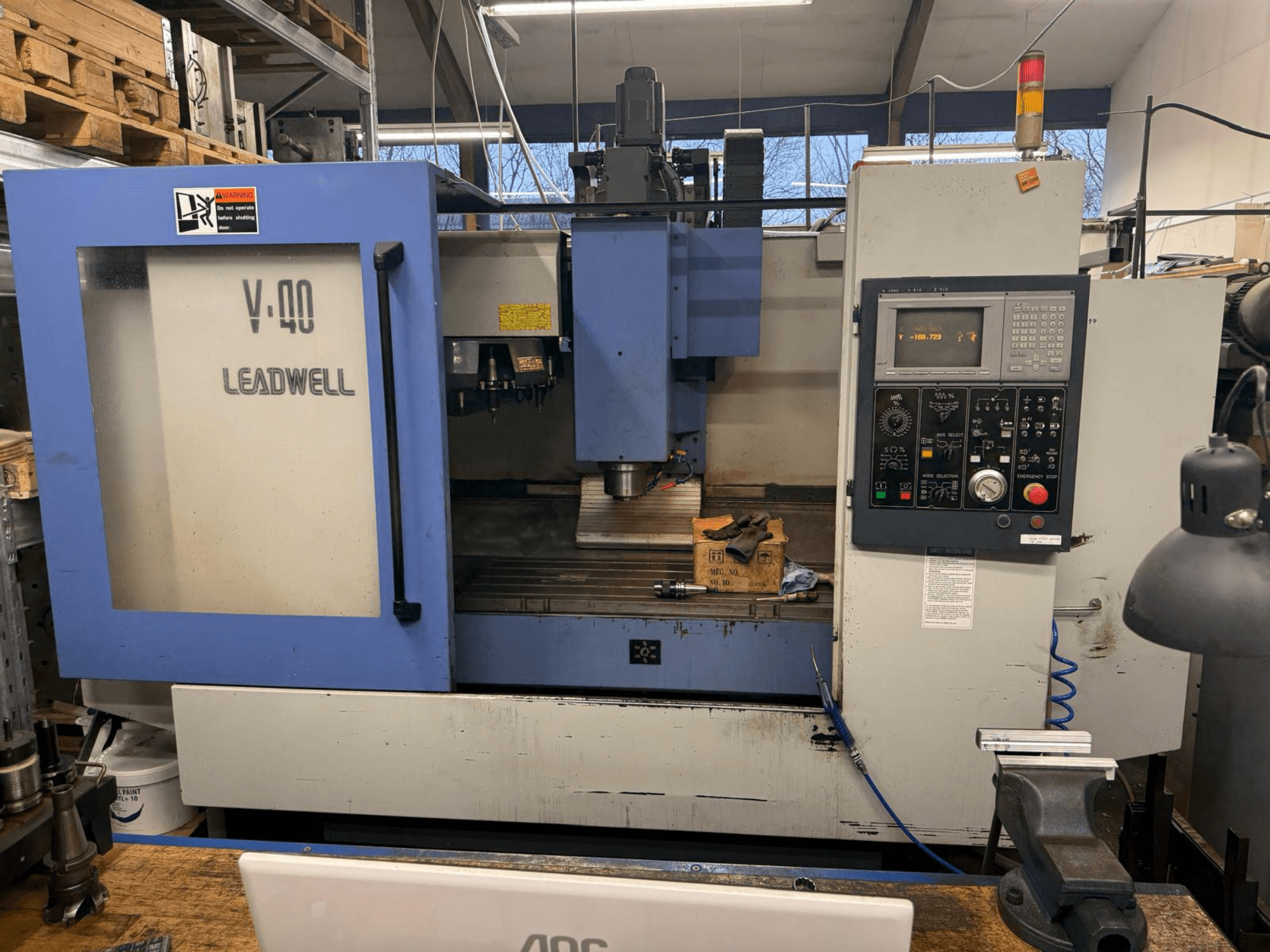 LEADWELL V-40 CNC freze makinesi, önden görünüm, bir kontrol paneli, kesme aletleri ve bir tezgah üzerinde bir mengene.