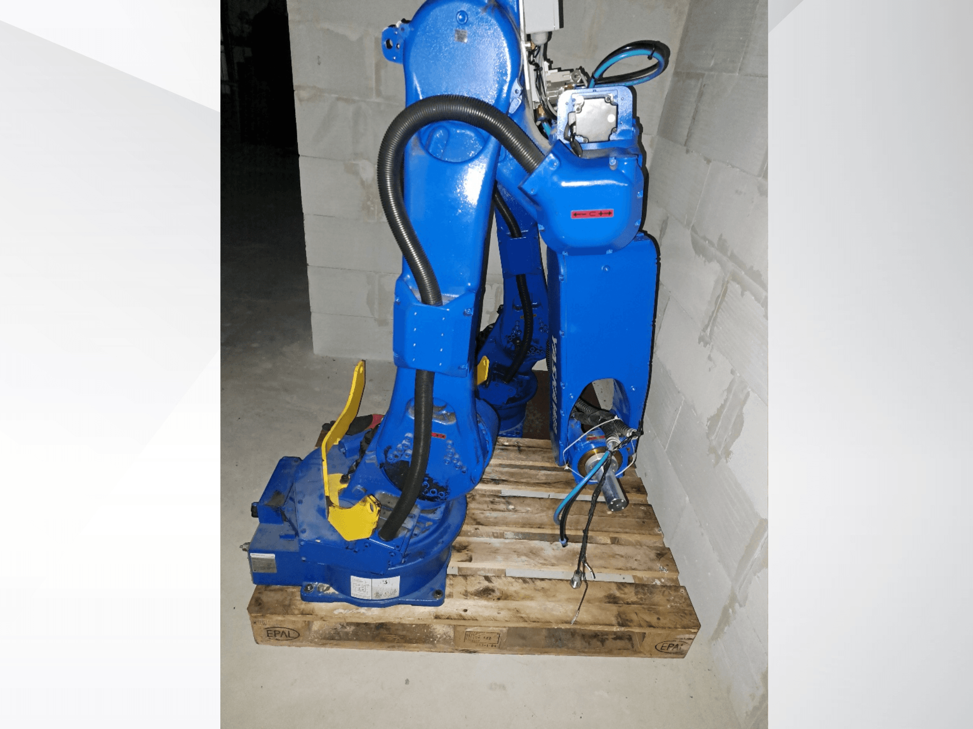 Mavi renkli Yaskawa Motoman GP25 robot kolu; ahşap palet üzerinde yan görünümde, kabloları ve mekanik eklemleri ile birlikte.