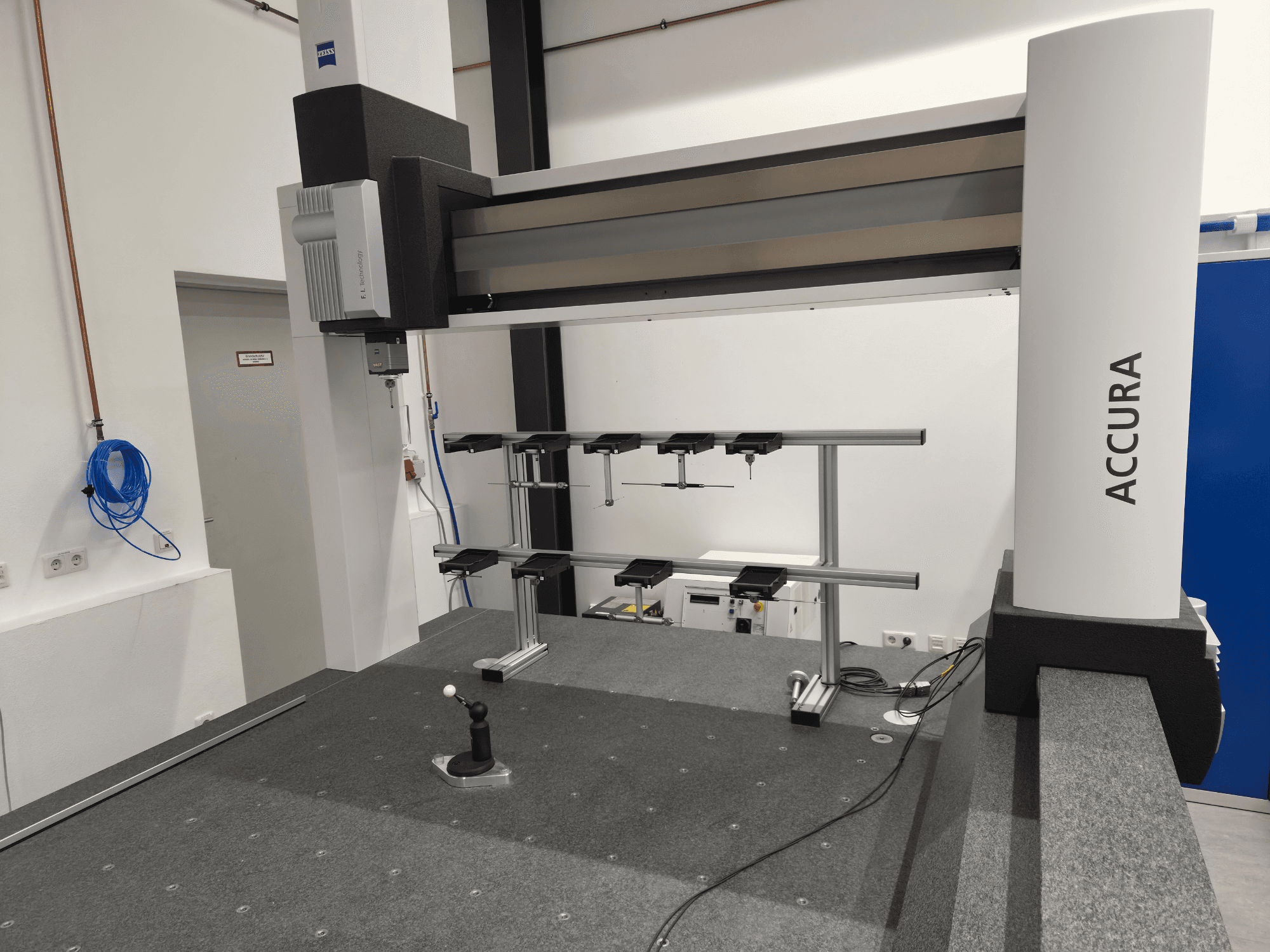 ZEISS ACCURA 16/24/10 CMM’nin önden görünümü; gri halı kaplı bir yüzey üzerinde ölçüm kolu, taban ve kontrol arayüzü gösterilmektedir.
