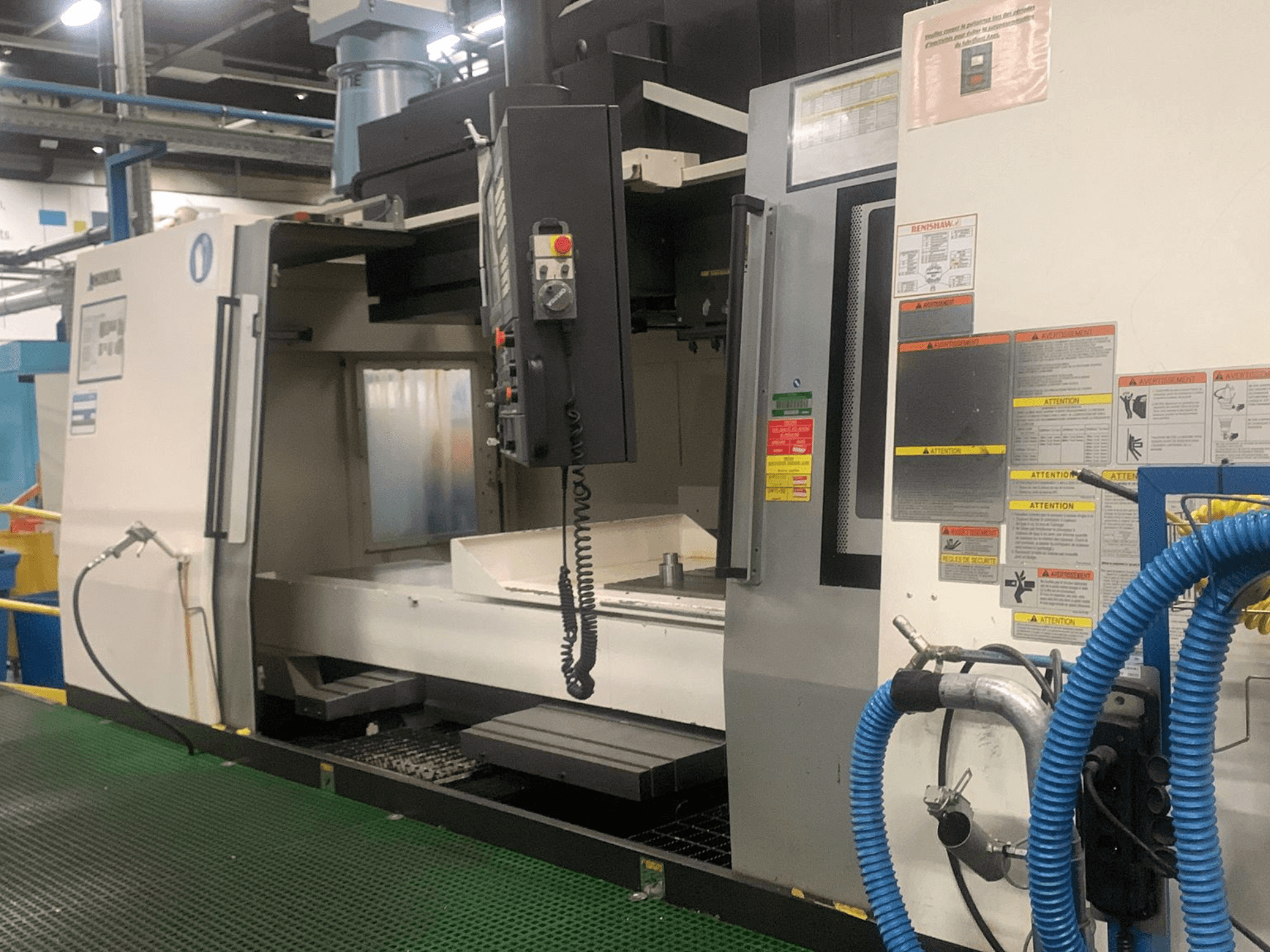 Okuma Millac 852 VII dikey işleme merkezi, önden görünüm; kontrol paneli, iş mili bölgesi ve güvenlik etiketleri gösterilmektedir.