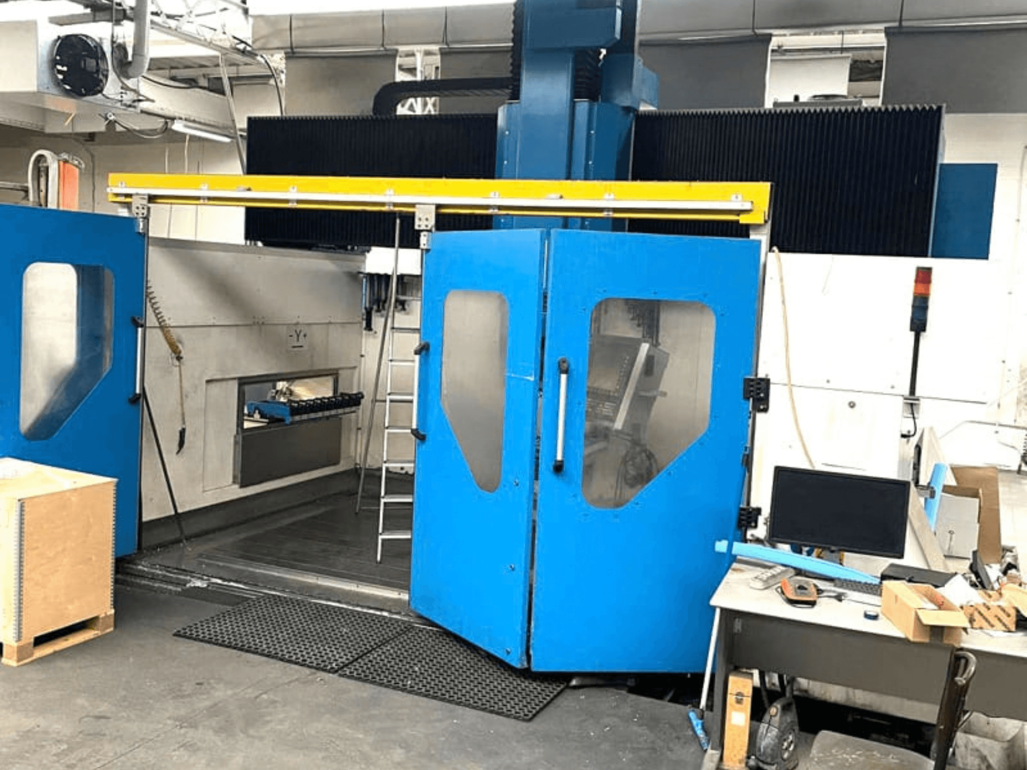 Mavi kapakları açık olan TECHMILL LABOR SHAPE 3220 dikey işleme merkezinin önden görünümü; iç kısımdaki çalışma alanı görünür durumda.