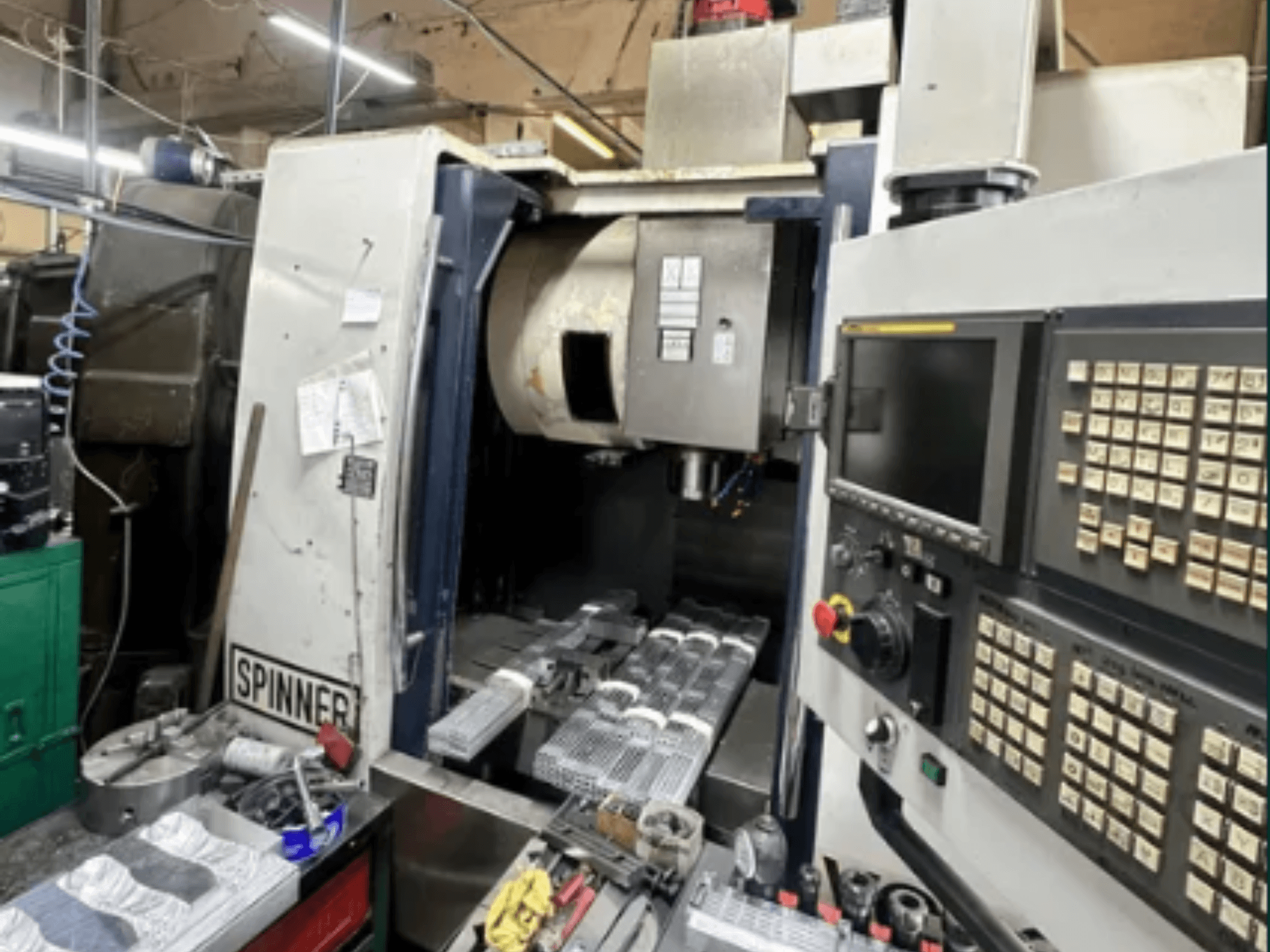 Spinner'ın CNC makinesi, önden görünüm; dokunmatik ekran arayüzü, çalışma alanındaki aletler ve işlenmeye hazır işlenmiş parçalar.