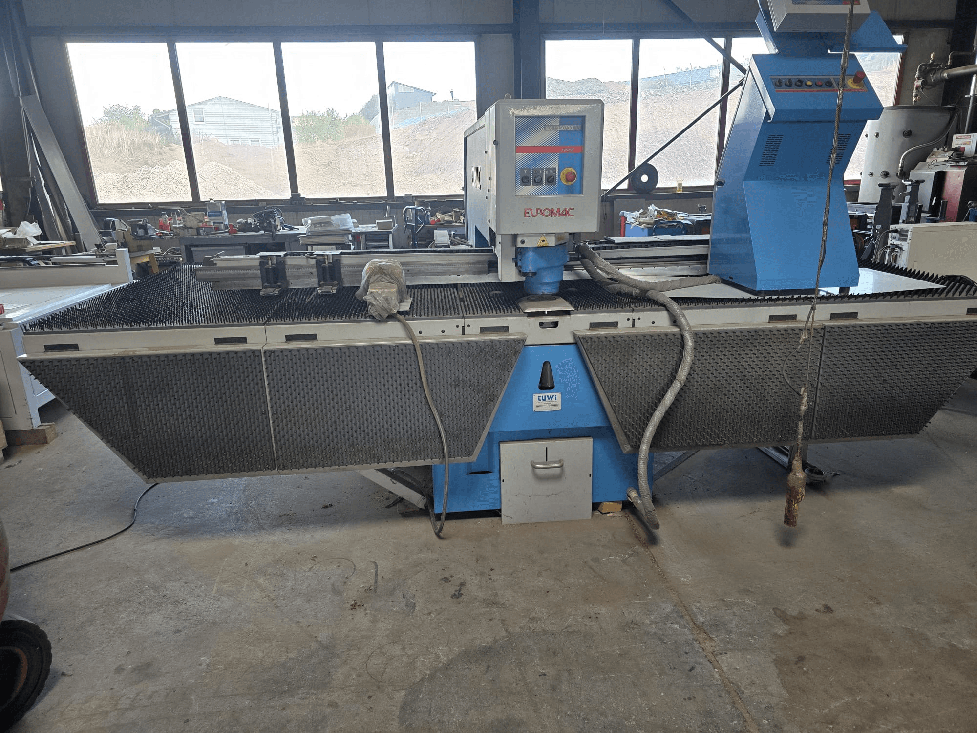 Bir atölyede bulunan Euromac BX 1250/30 CNC delme makinesinin, takım kumandalarını, endüstriyel tasarımını ve metal kesme yatağını gösteren yandan görünümü.