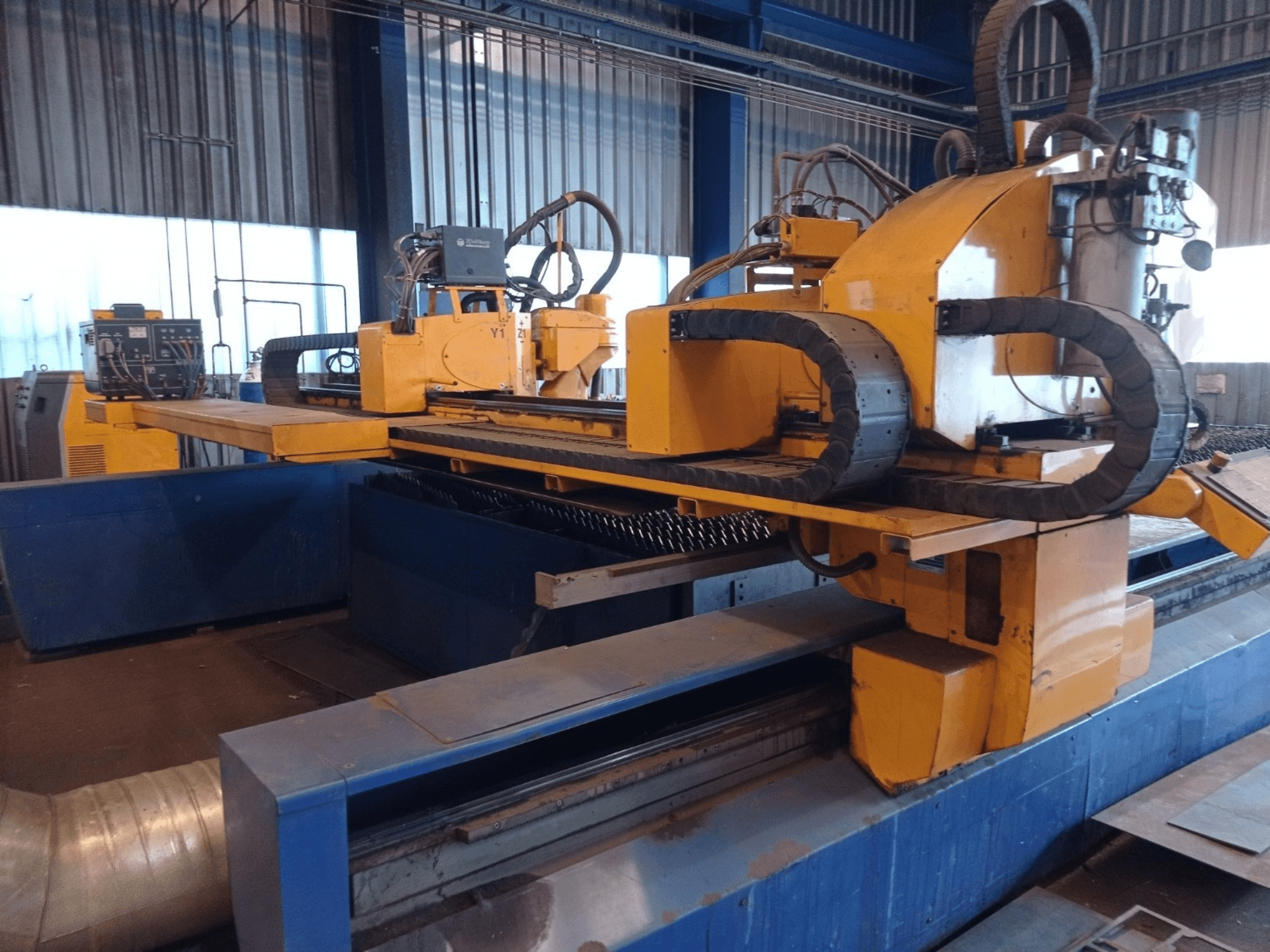 Kontrol paneli ve kesim yatağı ile önden gösterilen iki yatay kollu sarı CNC plazma kesim makinesi.