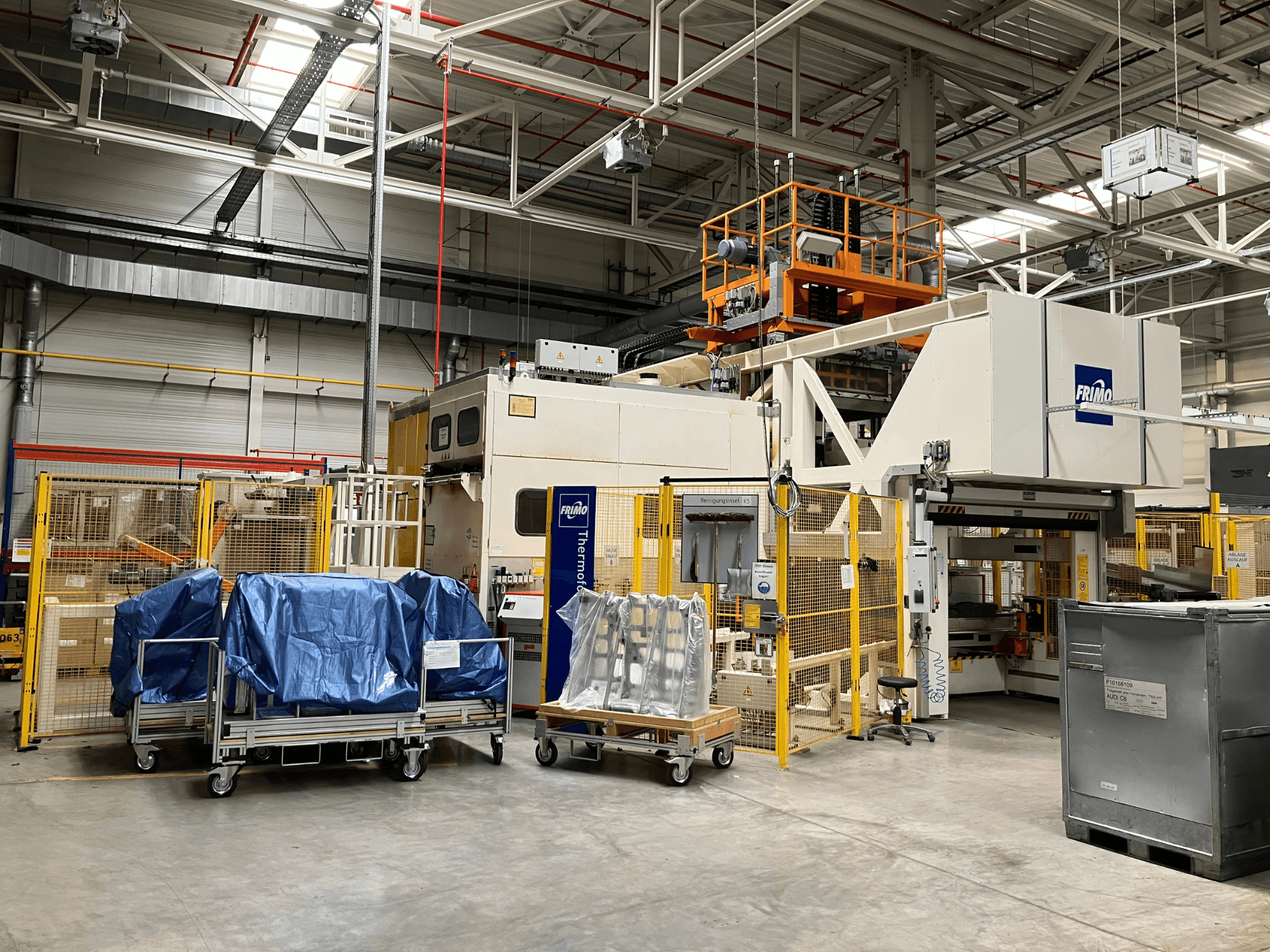 Bir fabrikadaki FRIMO FTL 80/200 Fullflex plastik işleme makinesi, mavi brandalar ve güvenlik bariyerlerinin göründüğü önden görünüm.