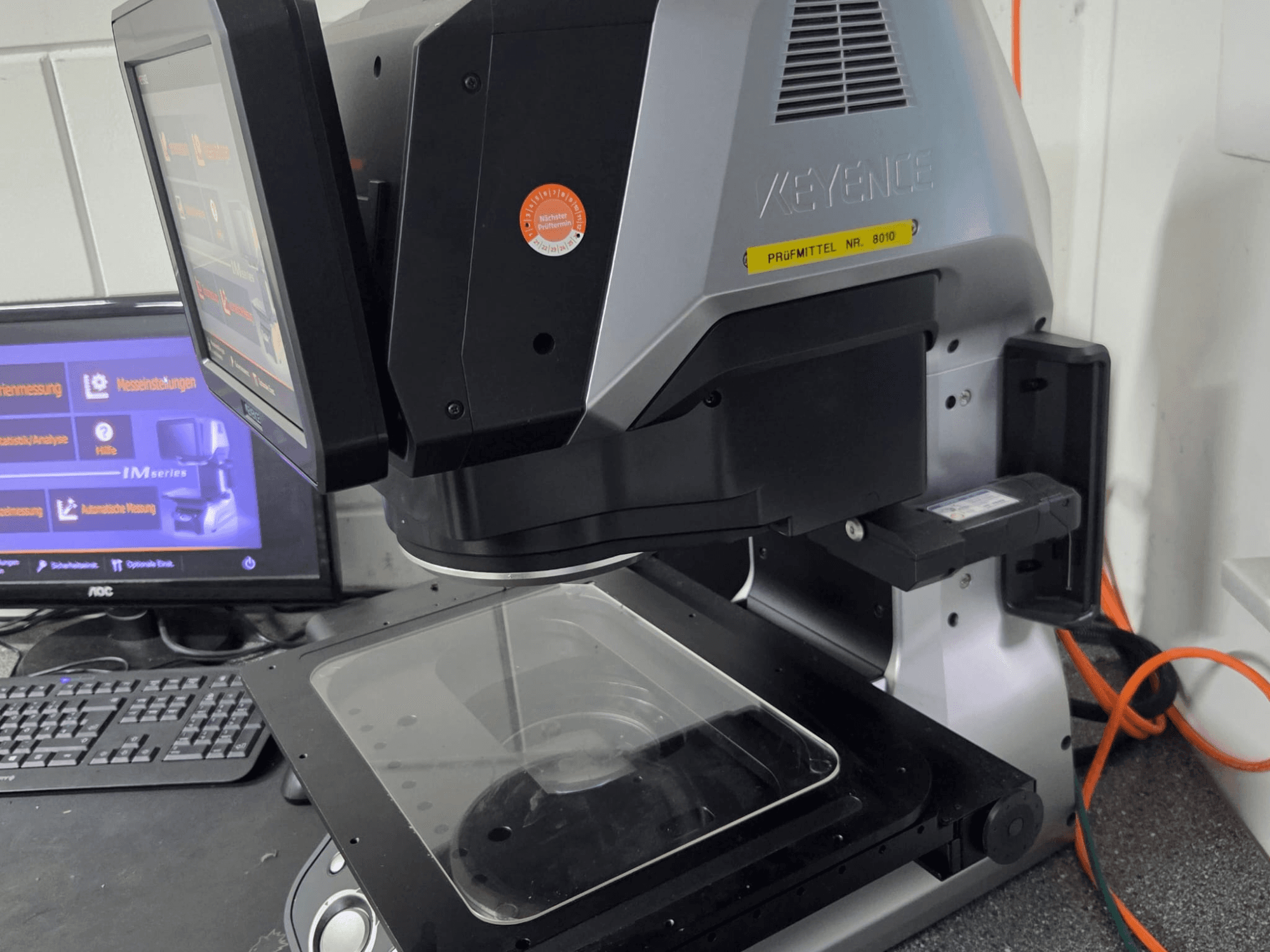 KEYENCE IM 7030 optik ölçüm makinesi, dokunmatik ekran ve cam ölçüm plakası ile önden görünüm.