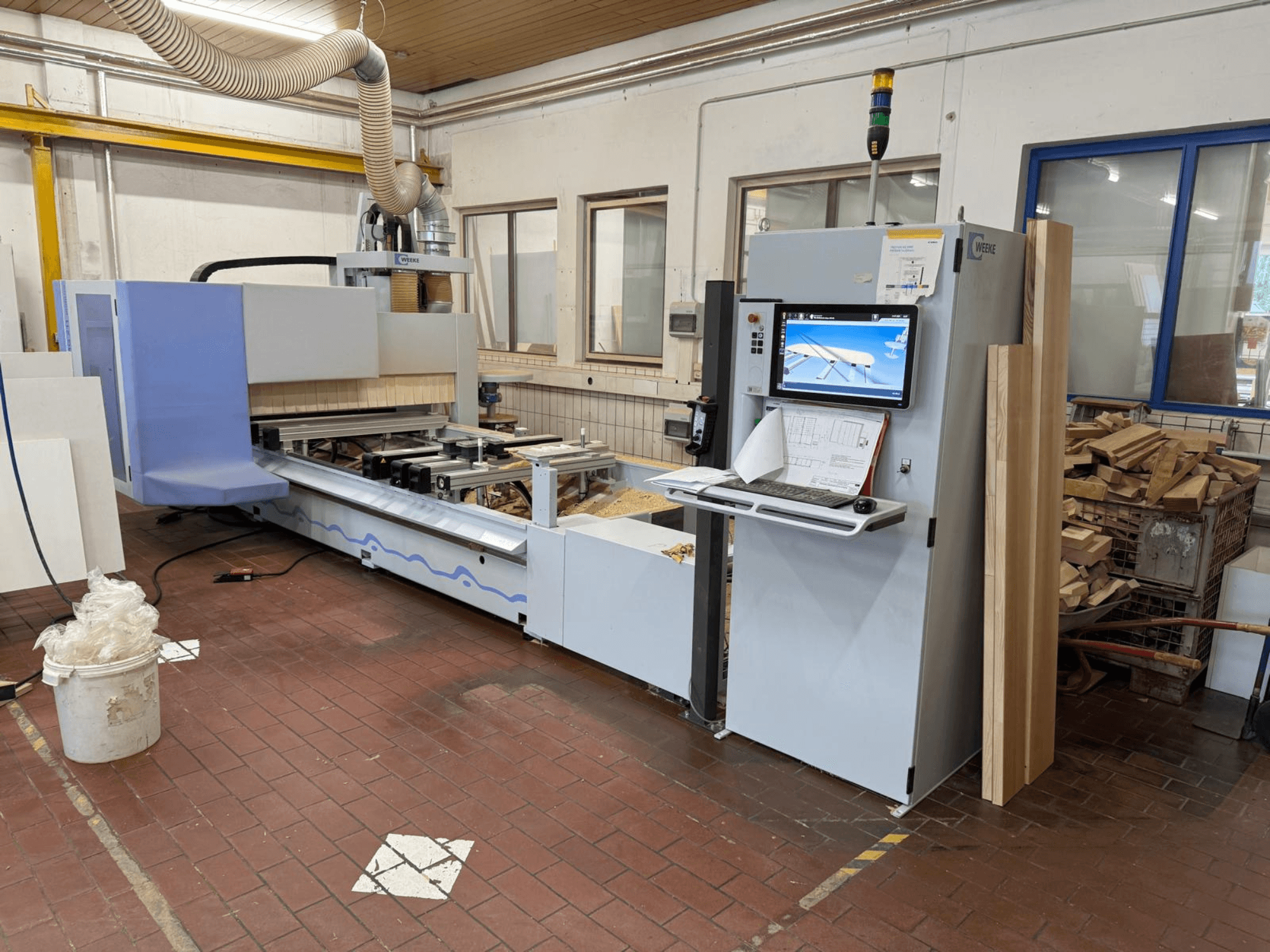 Weeke PROFI BMG211/32/12/K CNC ahşap işleme merkezi, önden görünüm; kontrol paneli ve ahşap parçalar ile birlikte, toz emme sistemi donanımlı.