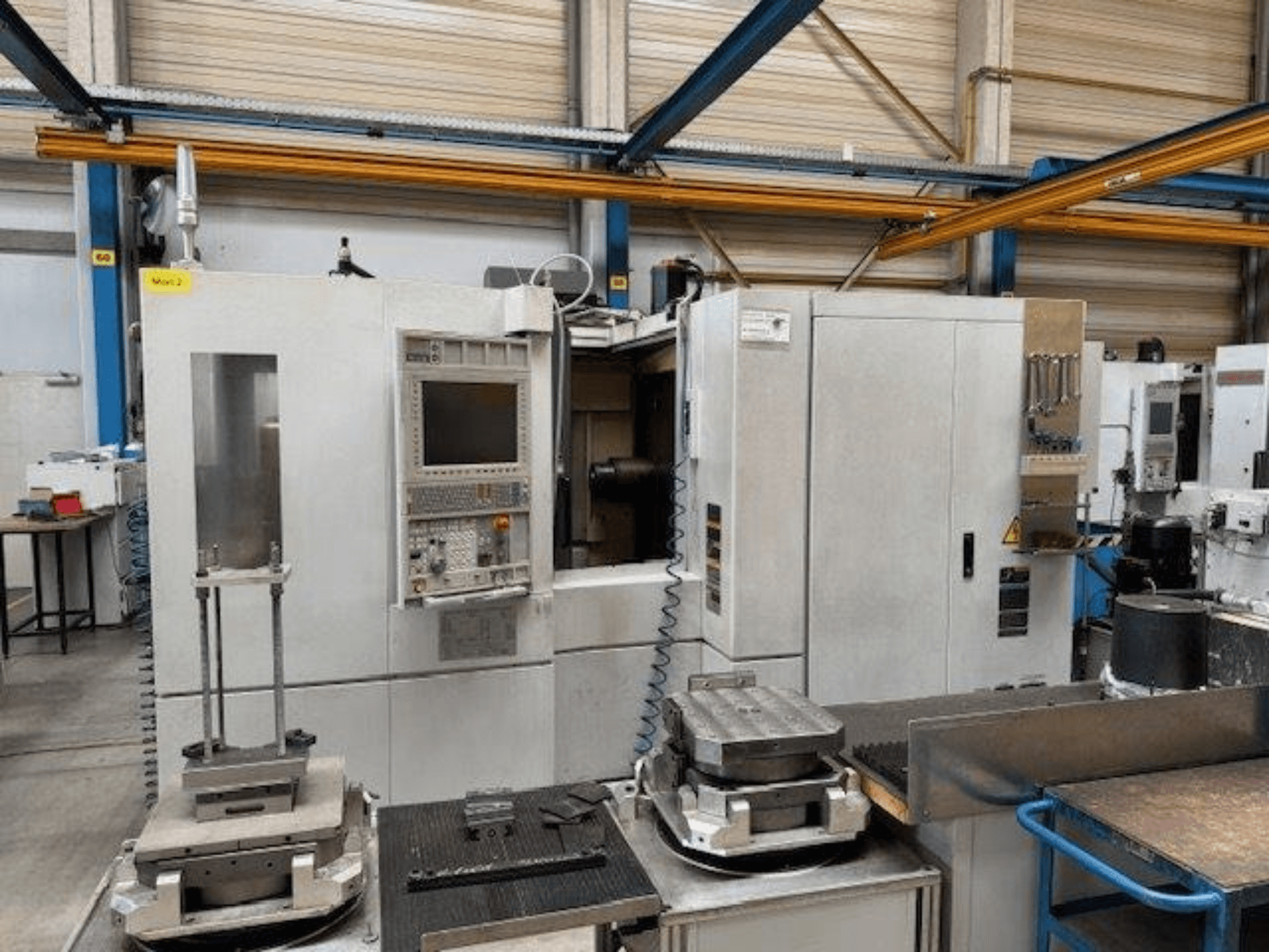 MORI SEIKI NH4000 DCG yatay işleme merkezinin kontrol paneli ve tabla üzerindeki iş parçaları ile önden görünümü.