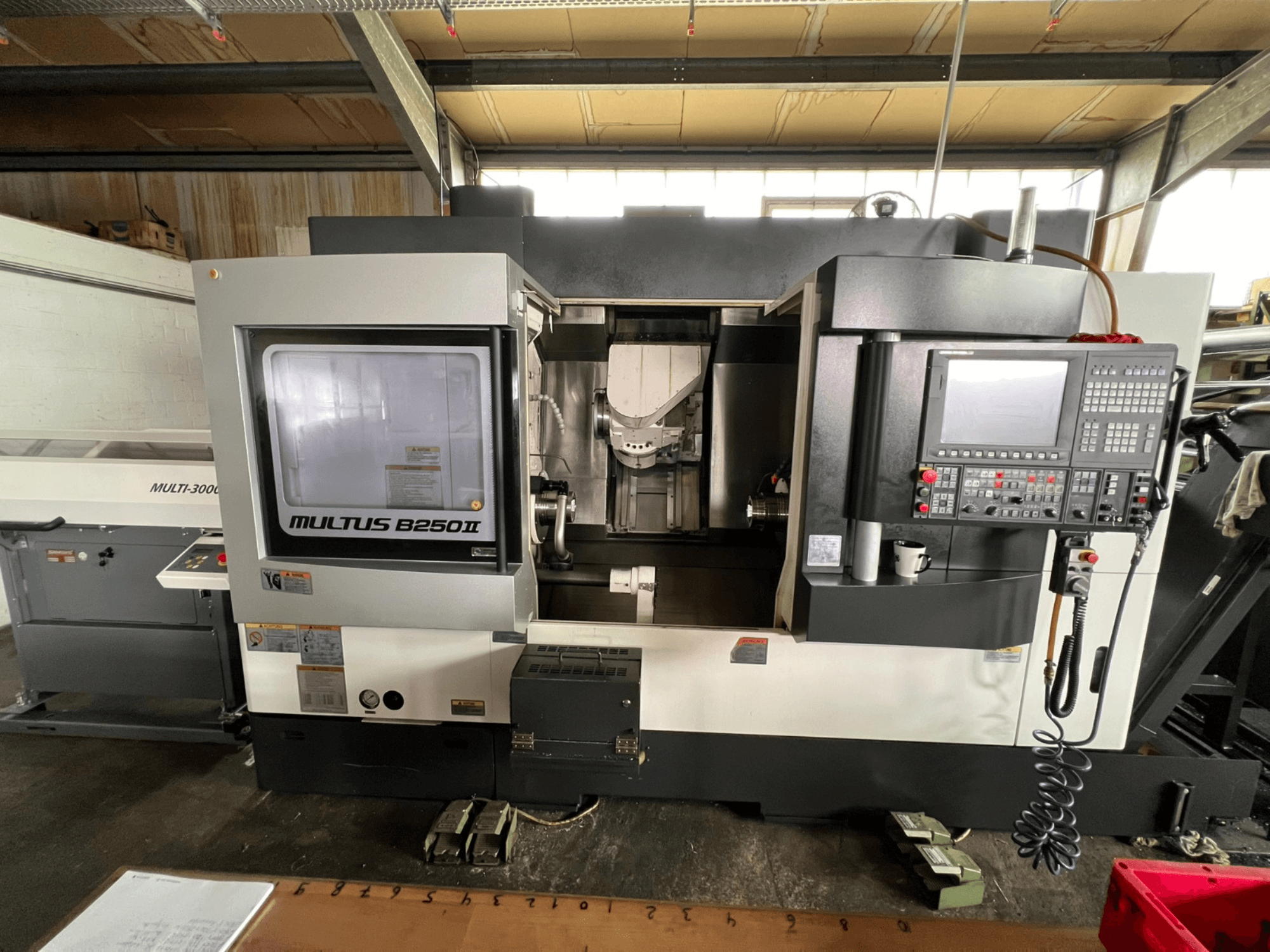 Okuma Multus B250II MW torna-freze merkezi, önden görünüm; kontrol paneli ve işleme alanı detayları gösterilmektedir.