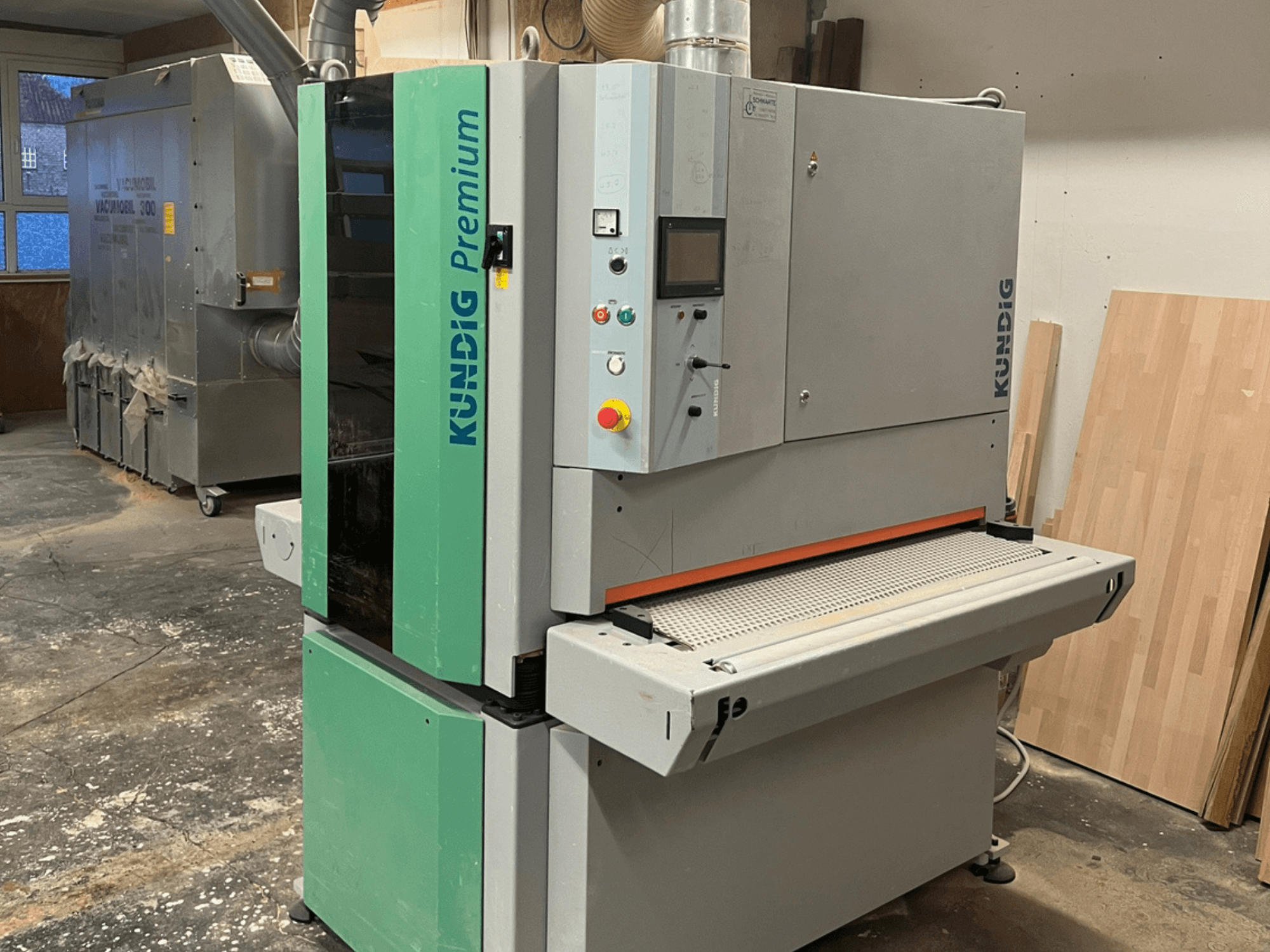 Gri ve yeşil renkli Kundig Premium-1 1100K bant zımpara makinesi, kontrol paneli ve zımpara bandı görünür şekilde yandan gösterilmiştir.