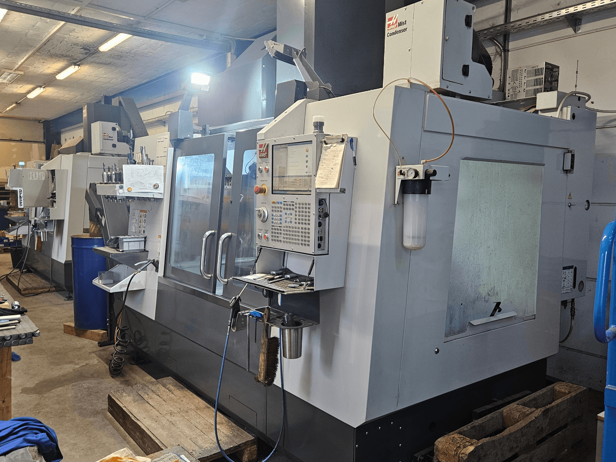Bir atölyede bulunan Haas VF-3YT/50 dikey işleme merkezi; kontrol paneli, takım tutucular ve sis yoğuşturucusunu gösteren önden görünüm.